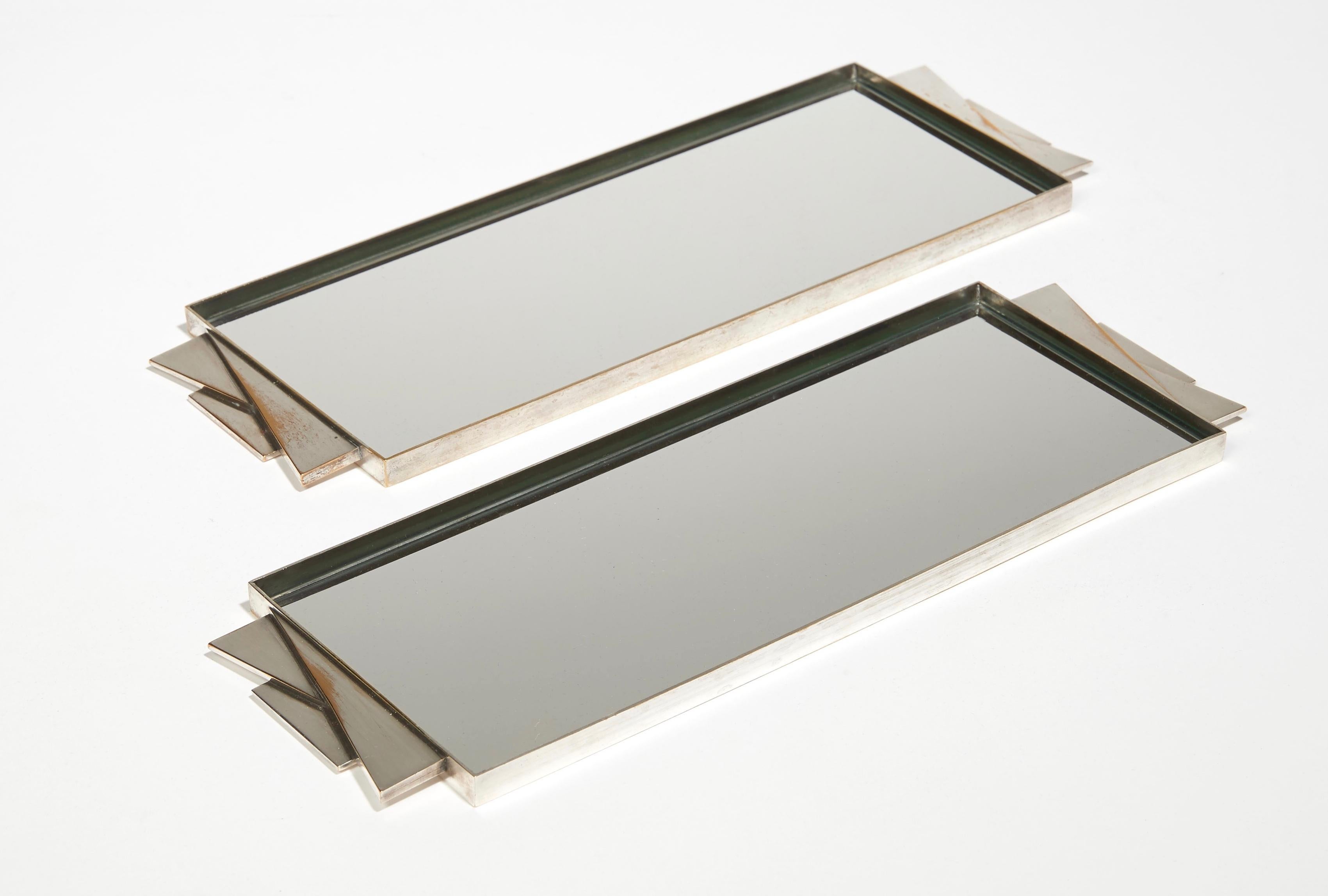 Set of two rectangular trays in silver nickel-plated metal with geometrical handles, enclosing a mirror. Each stamped with 
