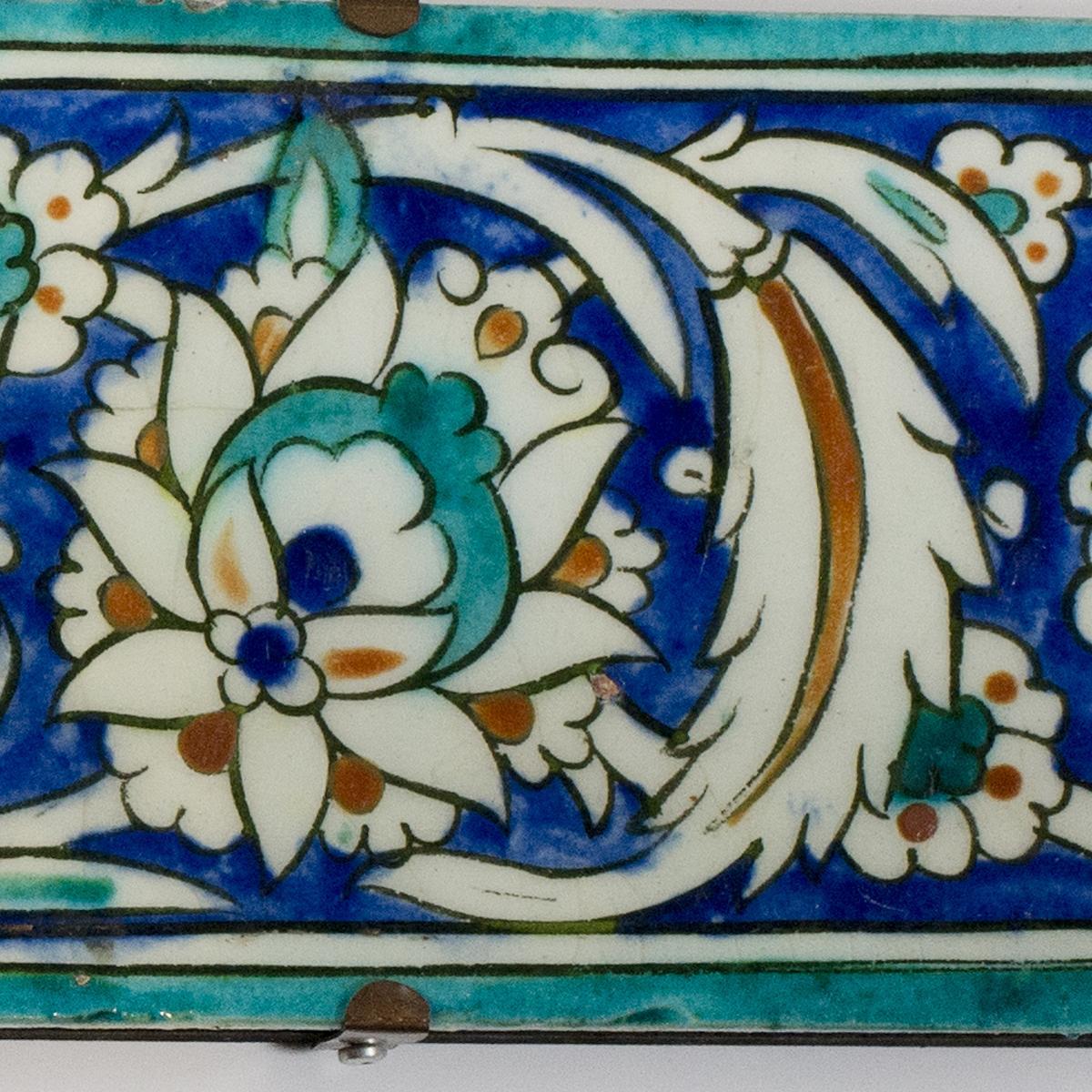 Two ottoman iznik border tiles, circa 1600, each of rectangular form, the glazed fritware painted in underglaze turquoise, cobalt blue, black and terracotta red with a continuous band of leafy arabesque scrolls enclosing flowerheads, with turquoise