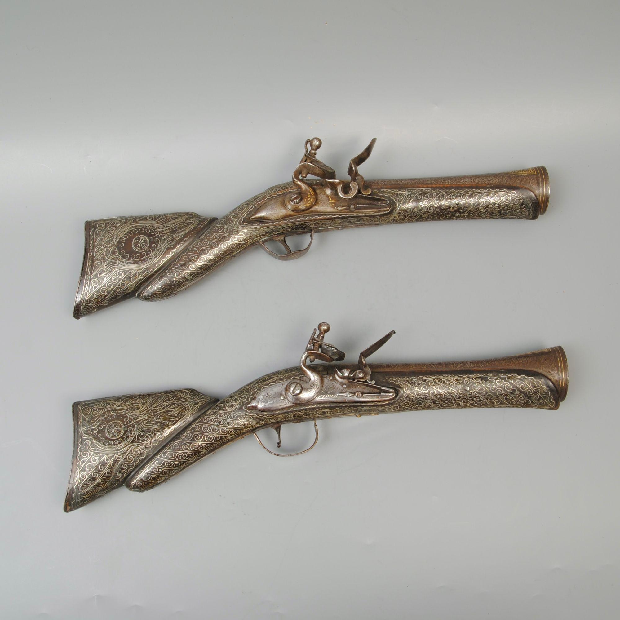 Two very similar examples make up this pair of super Turkish flintlock knee blunderbusses, both profusely inlaid with silver wire and with damascened barrels. Most examples have an Italian lock bought in by the makers of these highly decorated