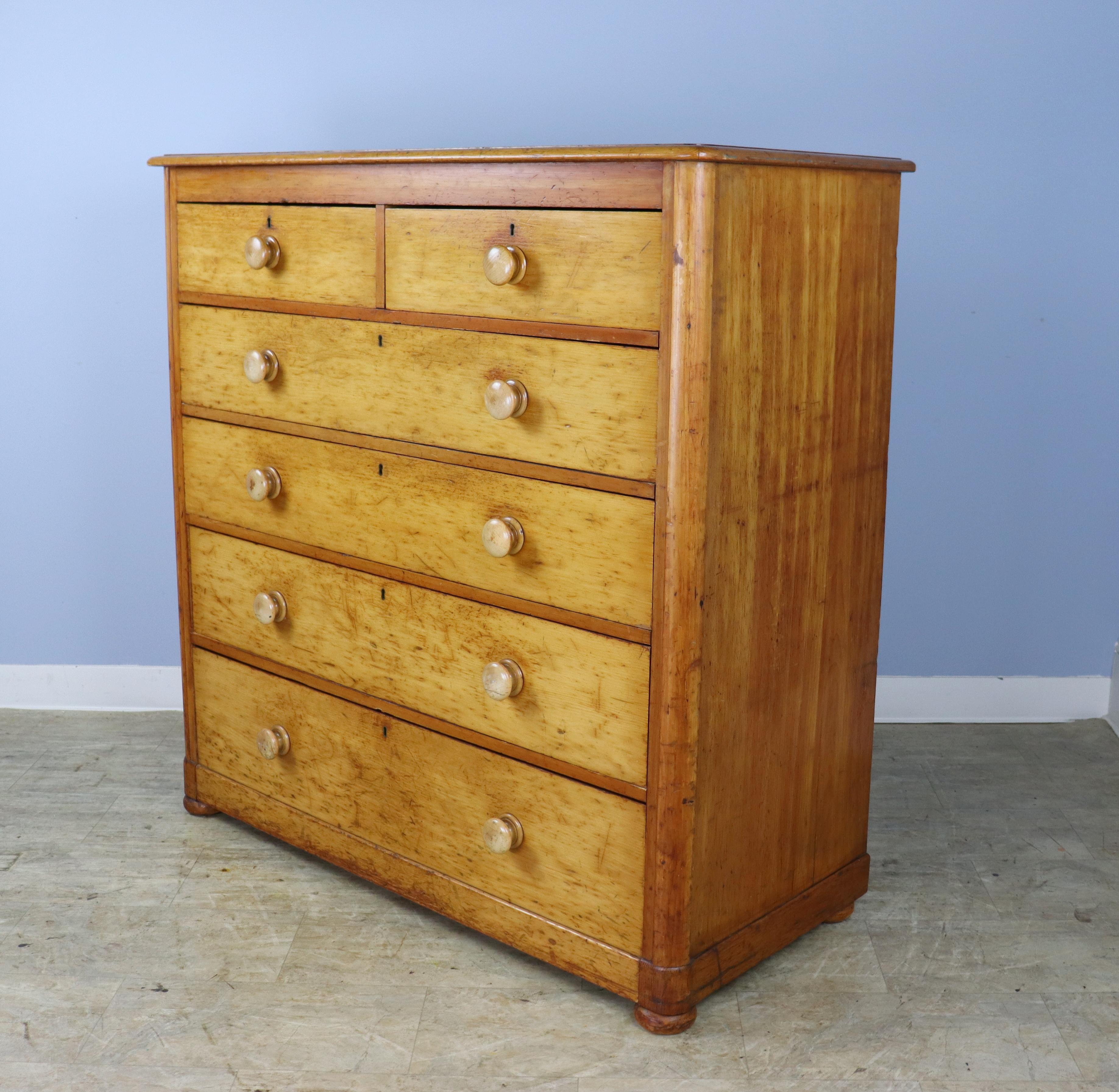 A tall 2 over 4 late Victorian chest of drawers in honey colored pine. While the exterior has lots of original old wear and distress, the interior of the drawers are clean and the drawers close nicely. Small fun feet add a charming note.
