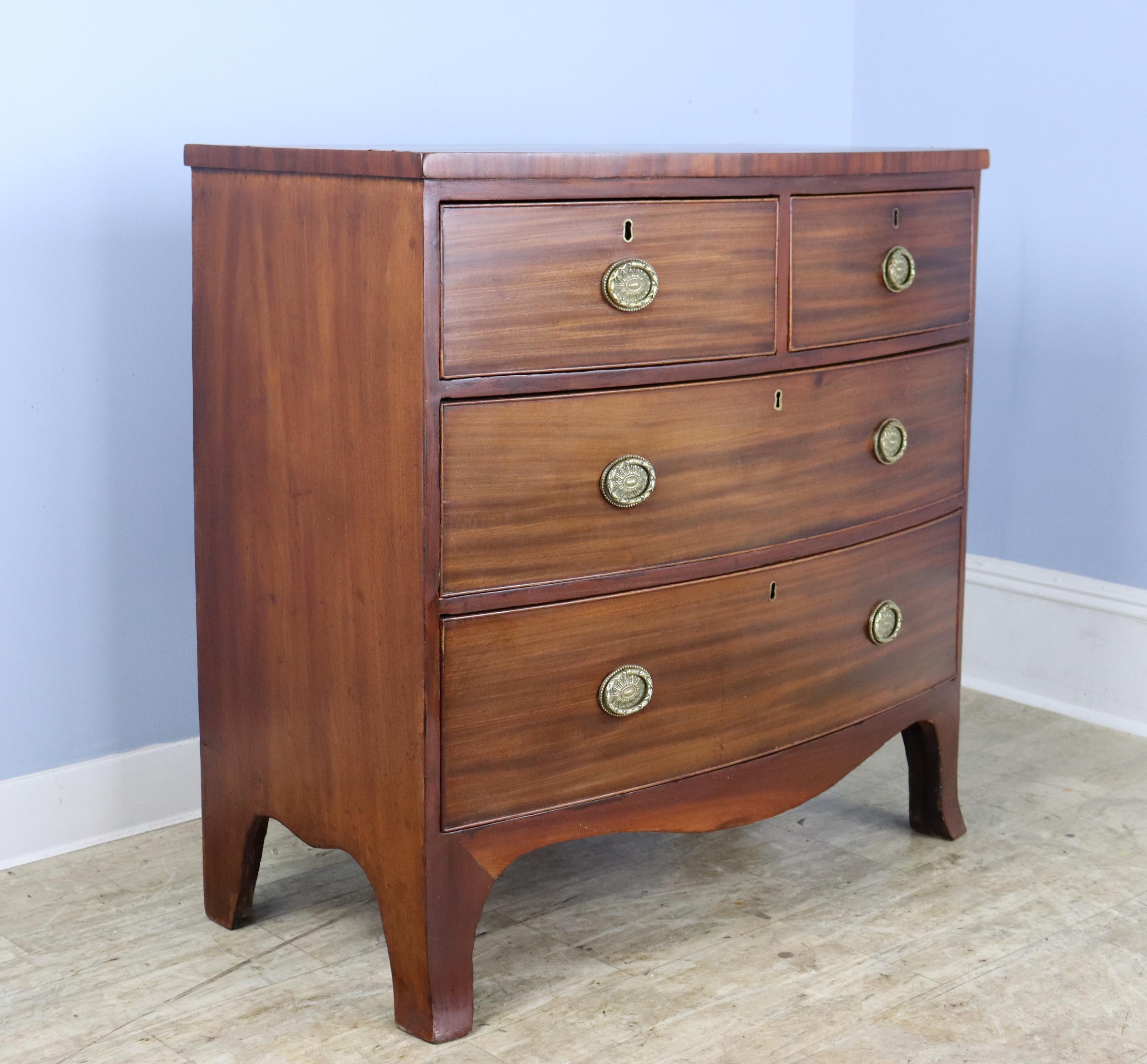 An antique bowfront mahogany bureau from England. Note the dramatic veneer around the tea-caddy top as well as the cockbeaded edging around the drawers, which are quite clean on the interior. The mahogany of this dresser has a beautiful grain and