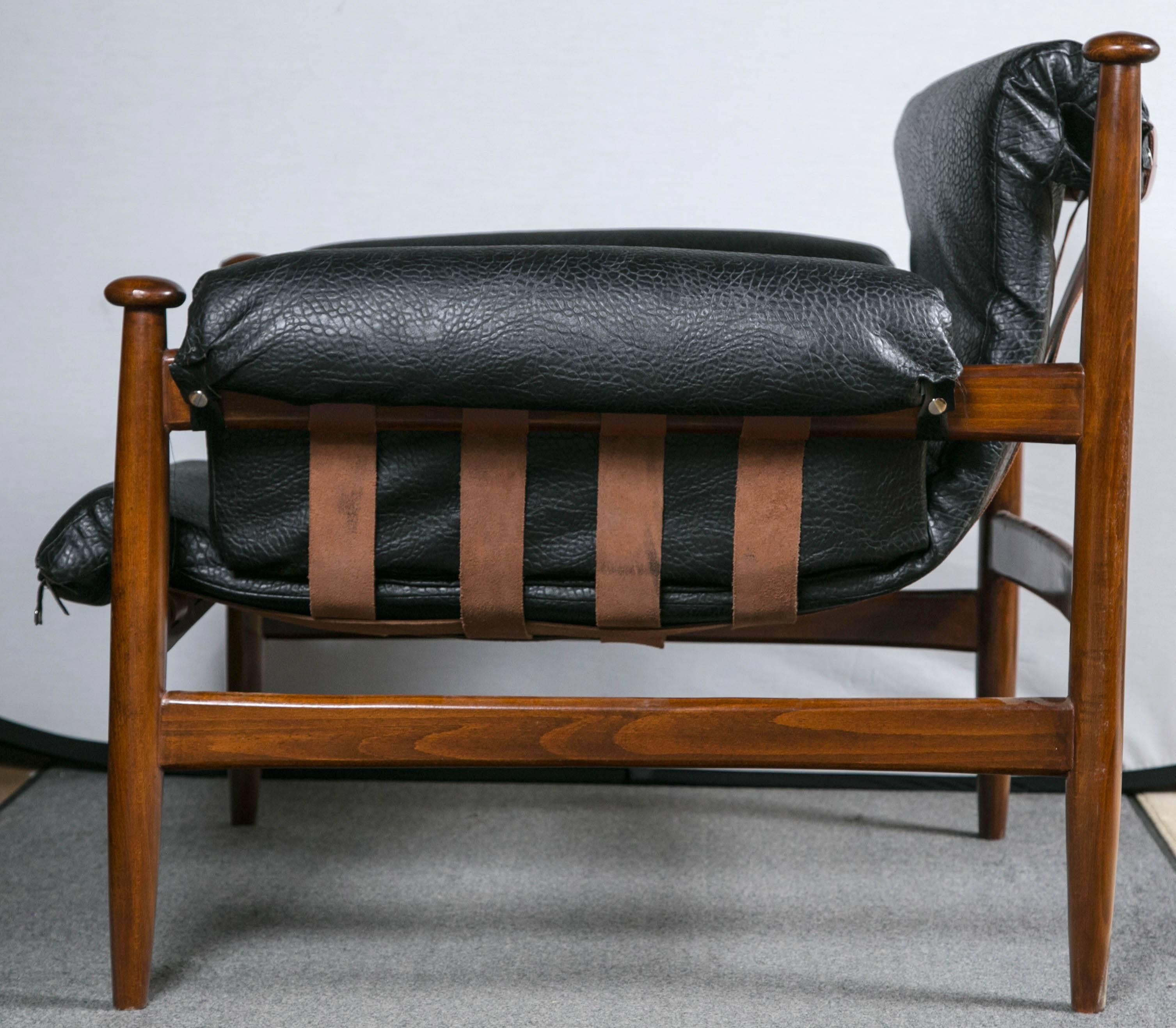 A fine pair of Finn Juhl designed this lounge chair, known as the bwana chair, in 1962. Its teak frame cradles a comfortable seat upholstered in rich olive blackish faux leather.