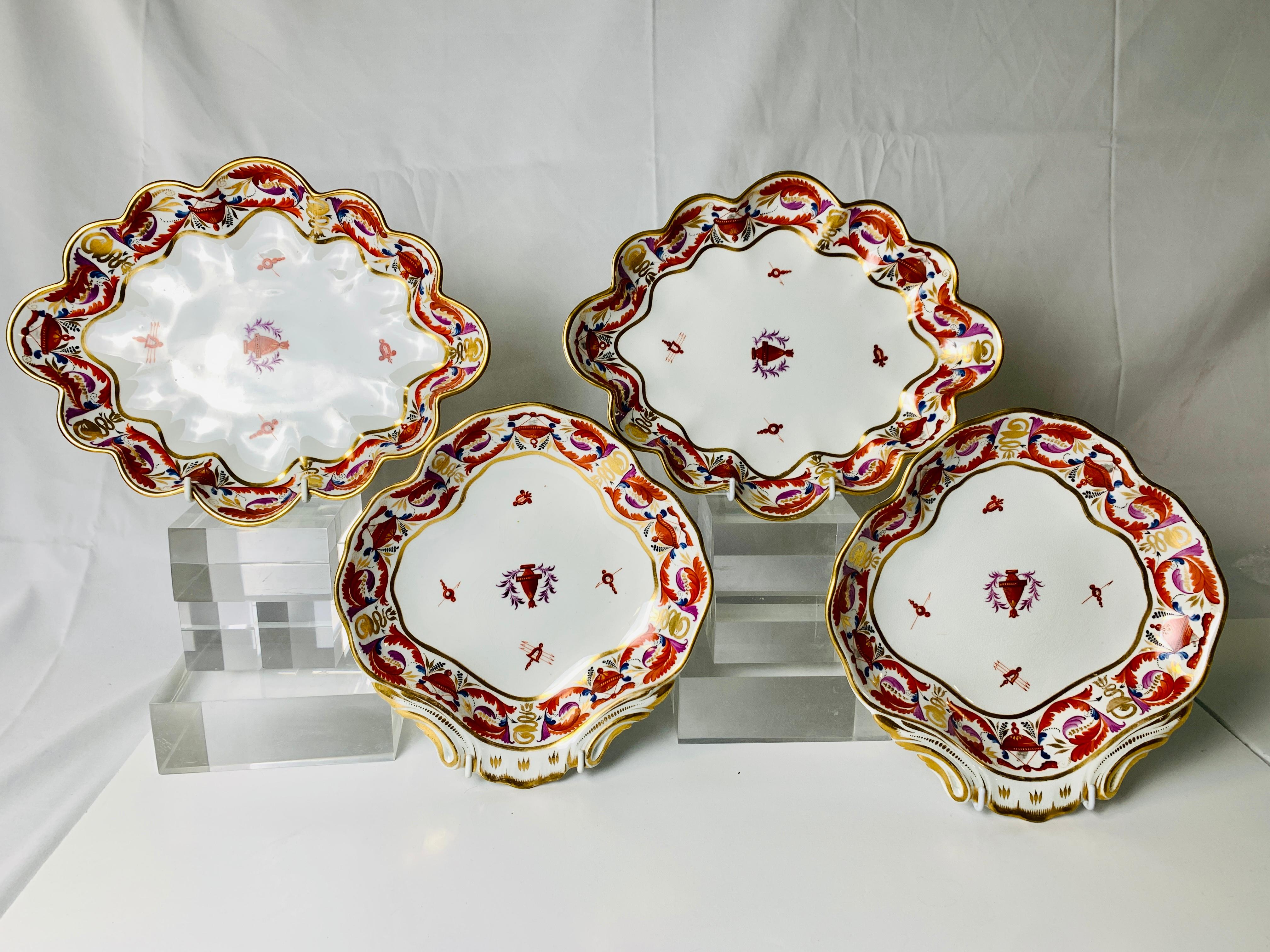 This group of four Derby Porcelain dishes was hand-painted in England circa 1810. An exquisite design of curling feathers and neoclassical objects decorates the borders. The color combinations are what makes these dishes so wonderful: red shading