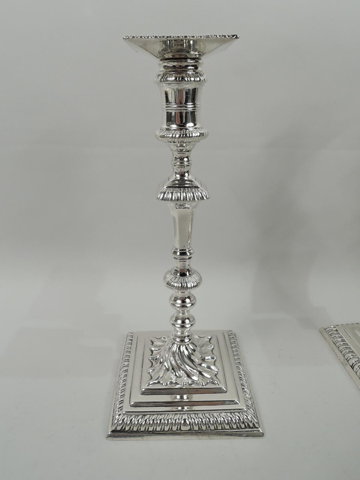 Two pairs of English Georgian sterling silver candlesticks, mid-18th century. Each: Spool socket with raised reeded girdle and square. Faceted and tapering shaft with flanges and knops flowing into raised foot with twisted fluted mount on stepped