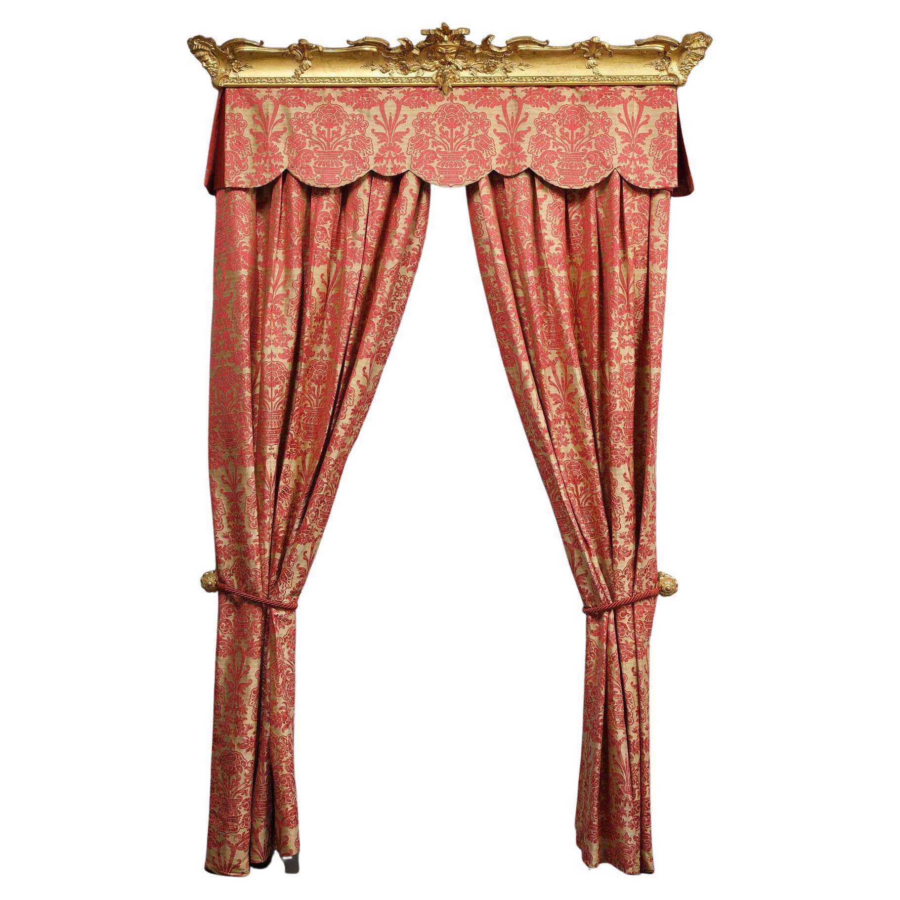Two pairs of Lucignano curtains by Fadini-Borghi and their valances topped by a gilded wood ramp molded and carved with masks and flowers. The curtains are cotton damask decorated with baskets overflowing with red flowers on a yellow background. The