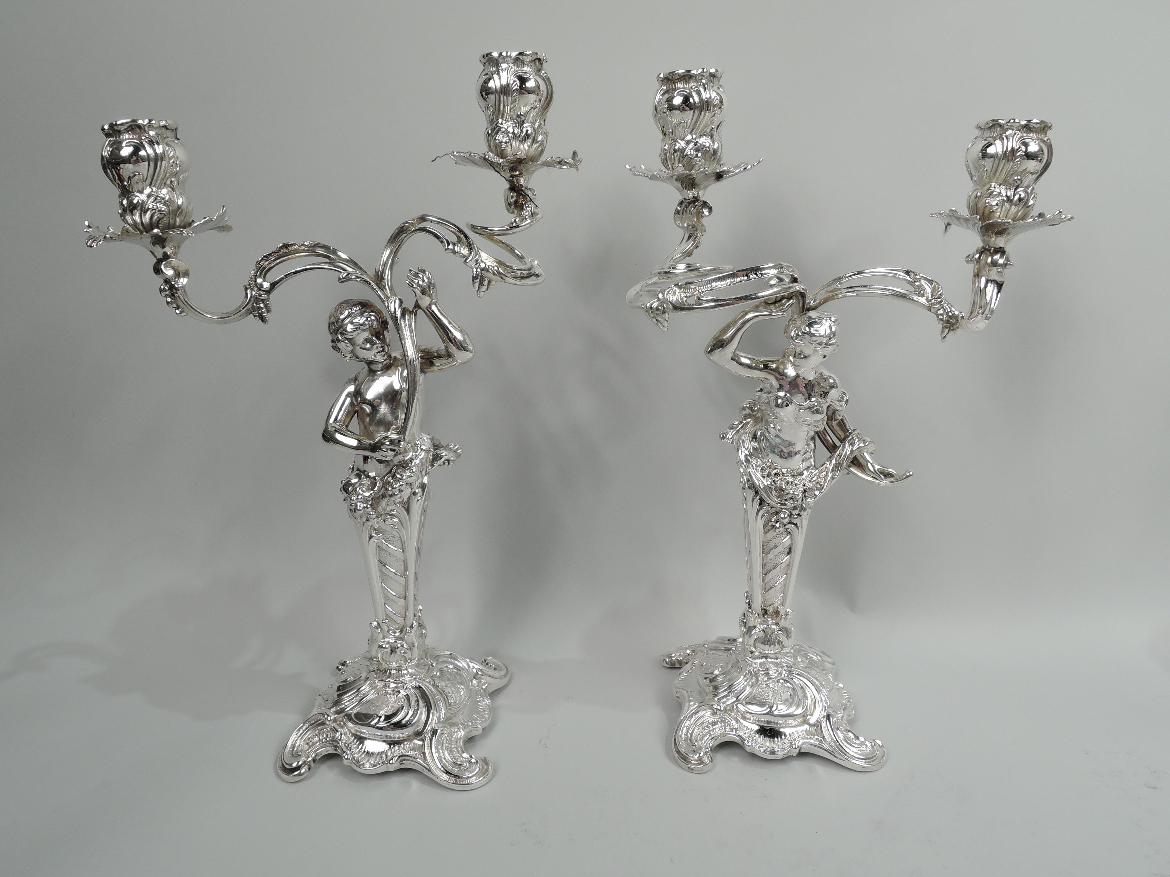 Two pairs of German 800 silver 2-light candelabra. Made by M. H. Wilkens & Söhne in Germany, ca 1890. Each: tapering pillar on raised foot with spread c-scroll supports. Garland-entwined figure mounted to pillar top. On two, a bosomy, drapery-clad