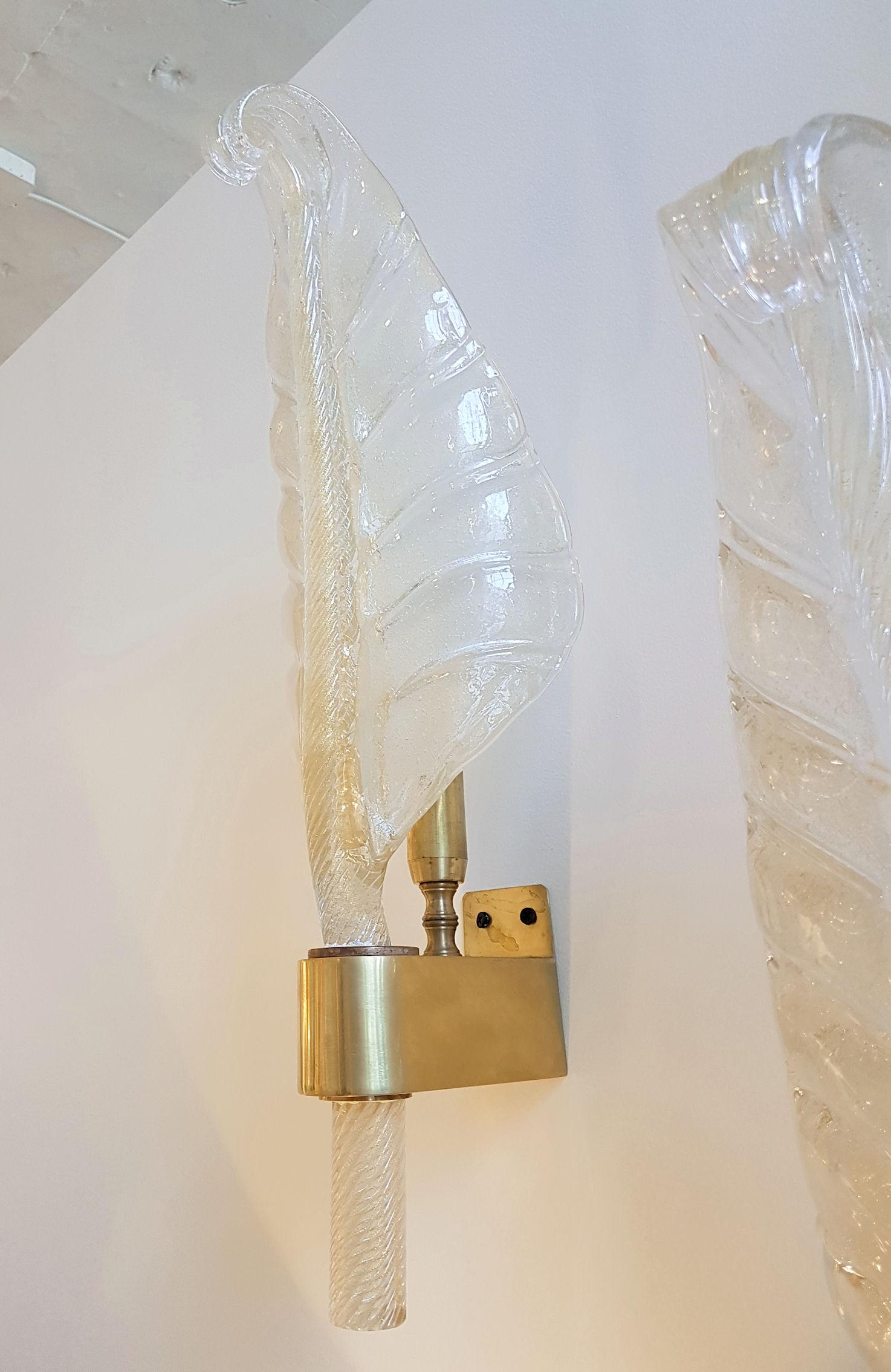 Two pairs of large gold flakes on clear Murano glass wall sconces, Mid-Century Modern.
The two pairs have brass mounts, 1 light each, and are rewired.
The 24 carats gold leaf coloration and the thickness of the hand blown glass, make the sconces