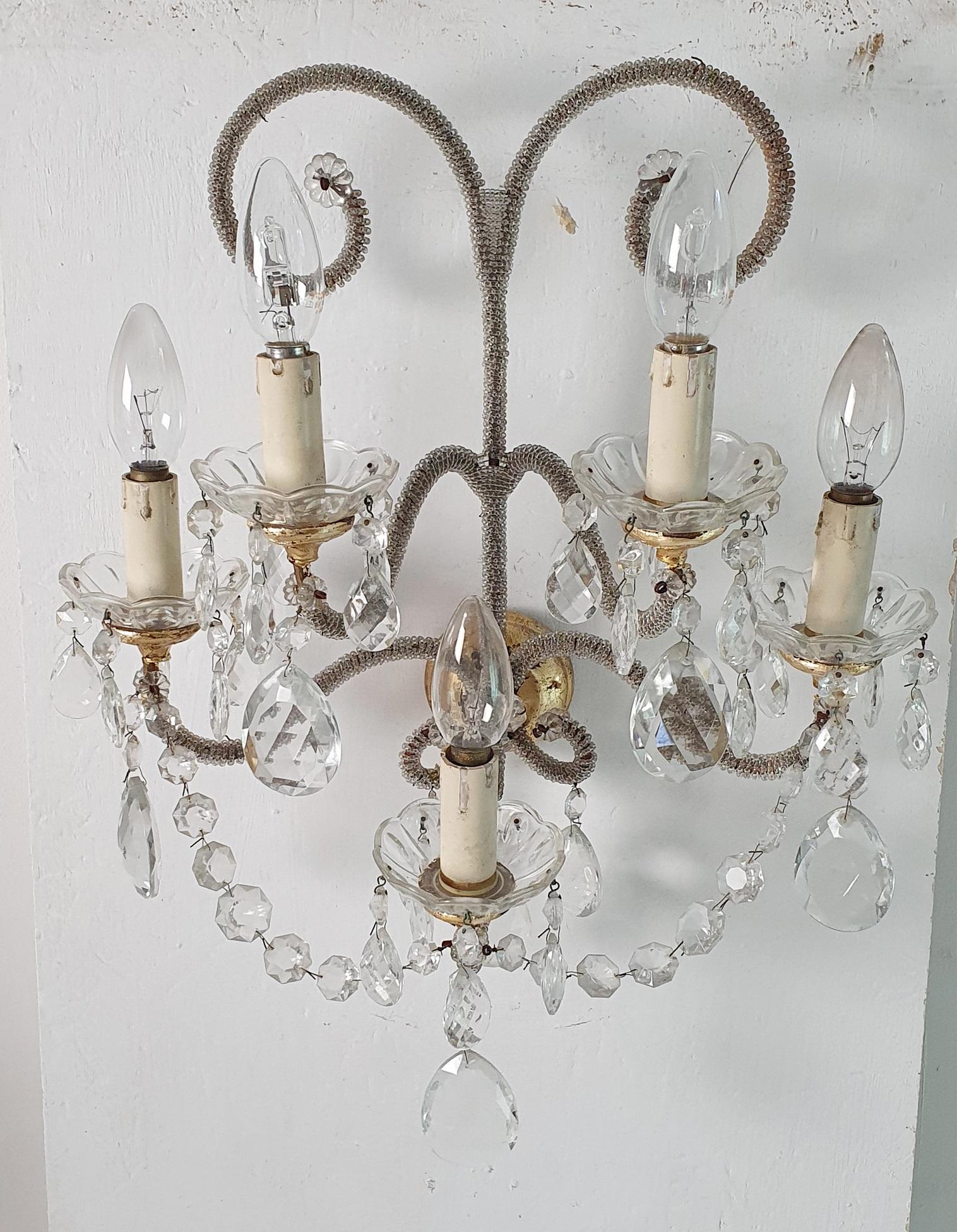 A pair of semi antique wall sconces in the manner of Maison Baguès. Each sconce has five candle style lightbulb holders and is decorated with clear and clear crystals and glass beads. The sconces are made from iron and painted in gold with added