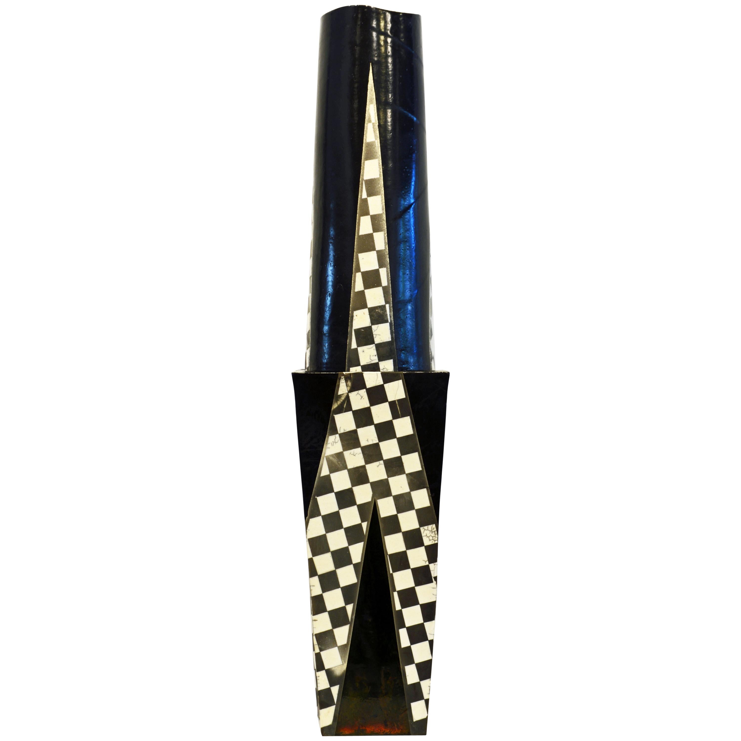 Standing more than 40 inches tall this epic Postmodern slab built glazed studio vessel or sculpture consists of a square tapering lower part with inlaid triangular checkerboard panels and slightly concave sides. On the top of this part there is a
