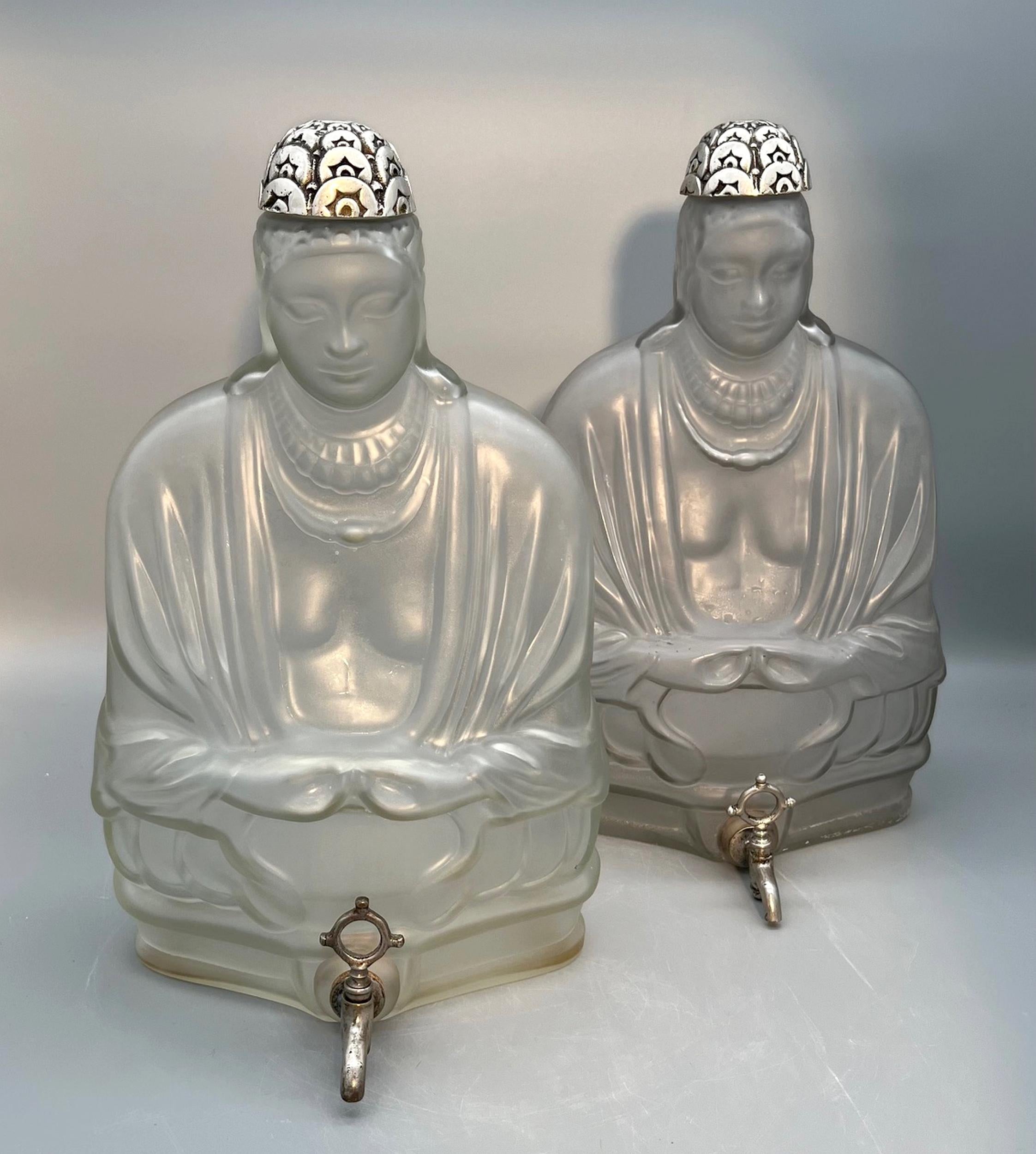 Due fontane di profumo in vetro soffiato e modellato, raffiguranti due Buddha.
Il coperchio, caratterizzato da un tappo a fiore, e il rubinetto sono in ottone argentato.

DALLA FABBRICA DI PROFUMI 