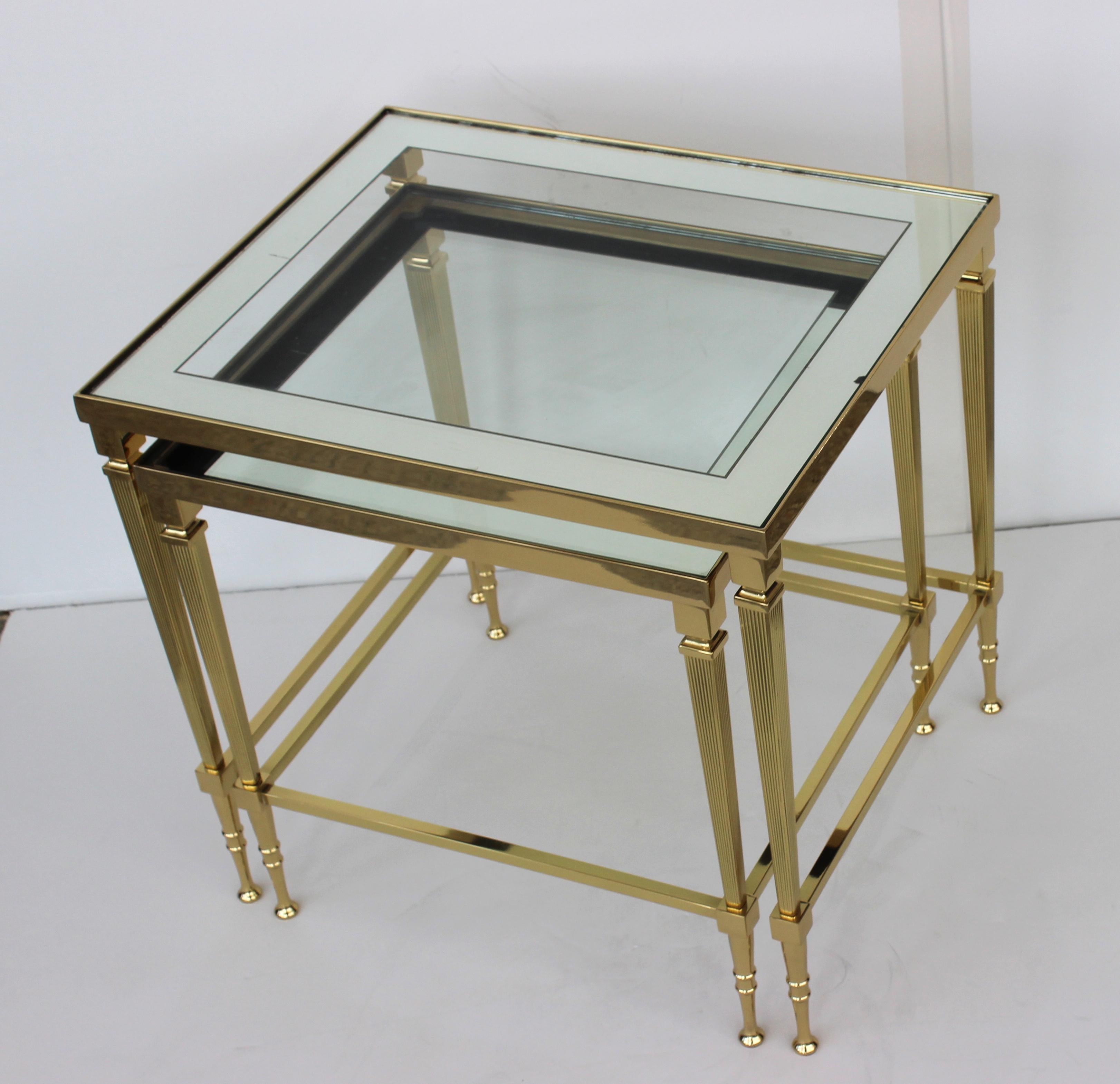 This stylish and chic set of polished brass nexting tables are attributed to Maison Jansen. The frames have been professionally polished and finished with a clear coat lacquer (no tarnishing), and they retain their original glass with mirror border