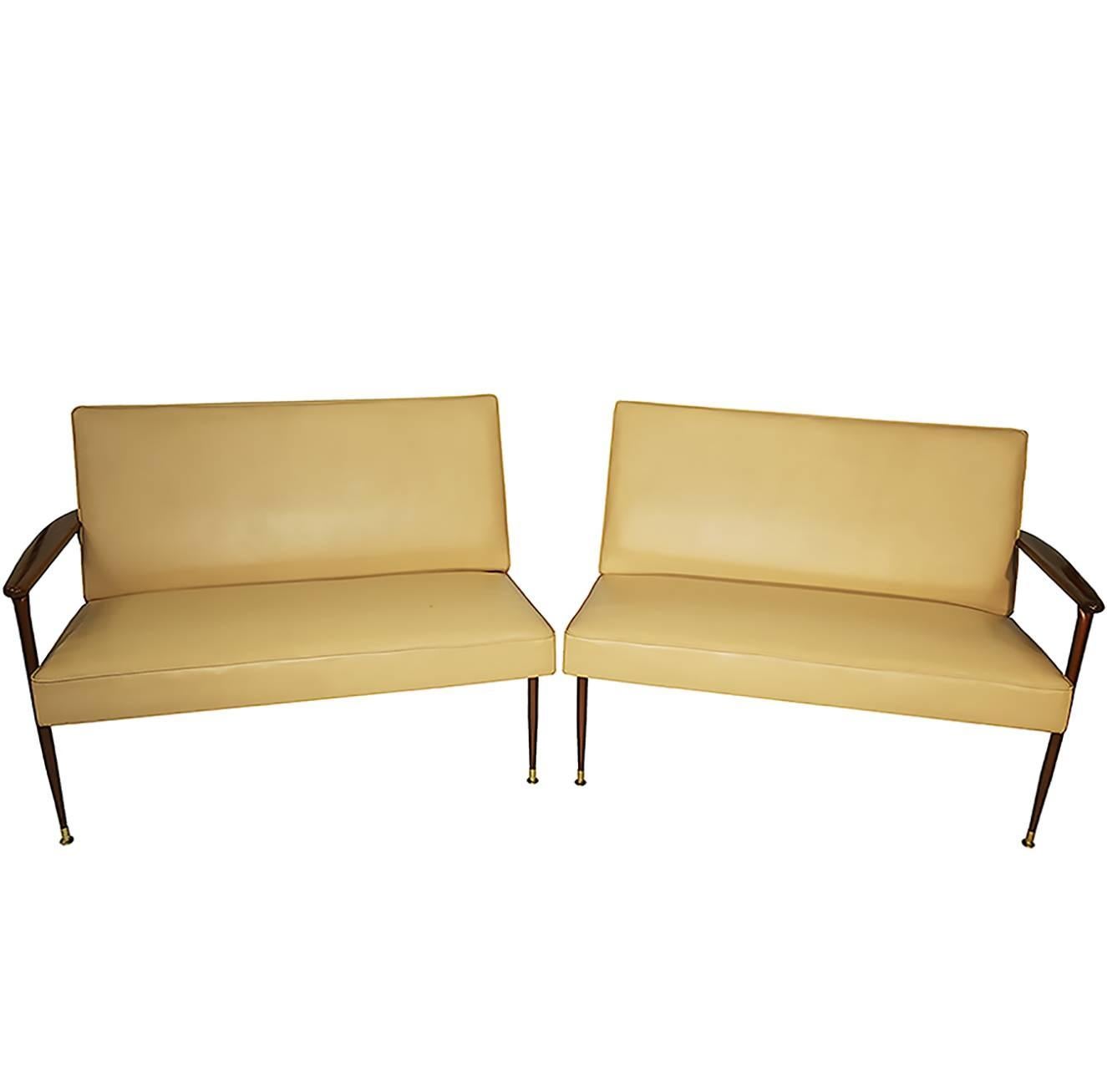 Two-piece sleek midcentury light cappuccino color faux leather loveseats with elegant shaped mahogany arms and legs. The legs end in elegant brass tips the loveseats can be placed together as a single sofa or used as two separate love seats. The