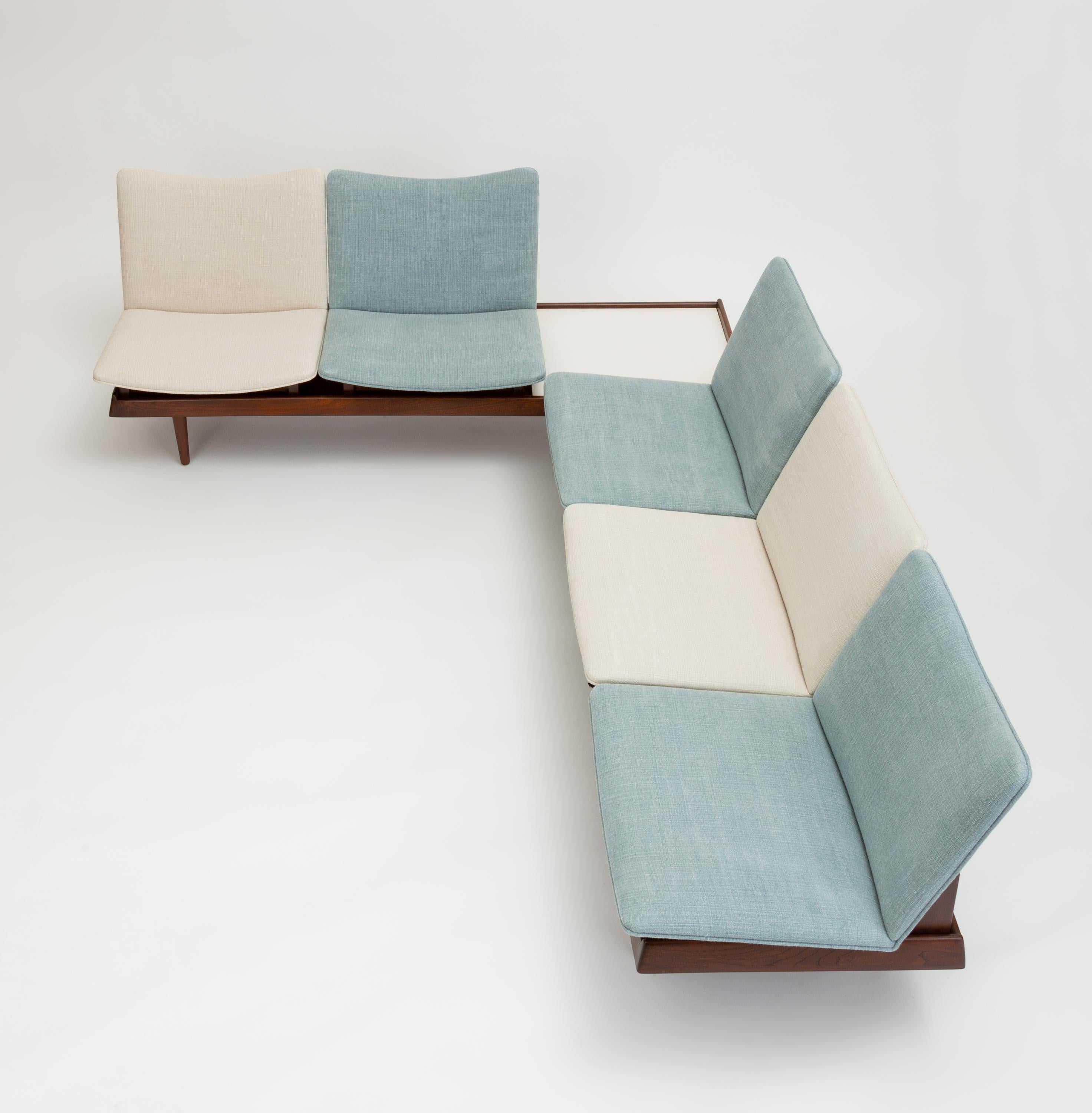 Two modular benches or small sofas with interchangeable seating modules and surfaces by California designer Gerald McCabe. Each piece has a low walnut base with raised edges and round, tapered legs. Each bench fits three modules. Included in the set