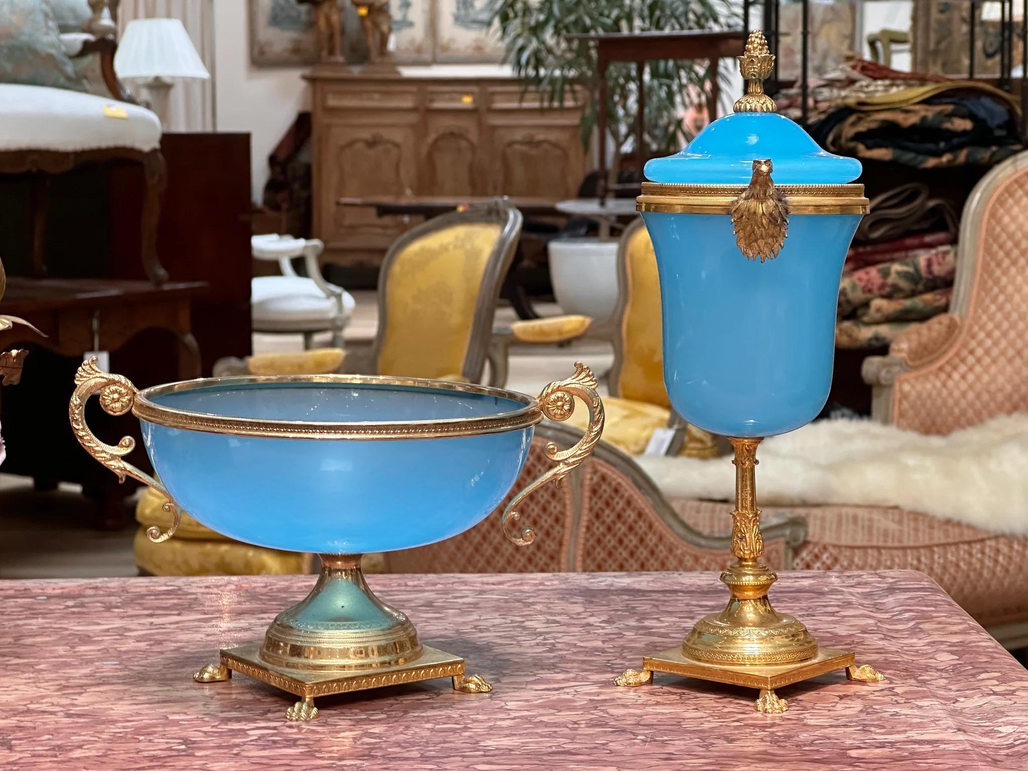 A two-piece set of French blue opaline, having dore bronze gilded accents, c. 1860, likely Palais Royale.   The urn has eagle head handles, and an acorn finial. The pedestal bowl has scrolled handles. The urn” 11 ¾” h.  x 7” w.  the bowl 5 ¼” h. x 9