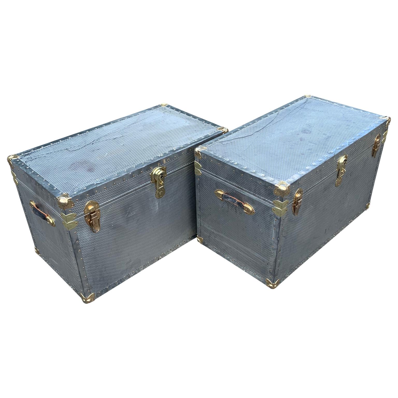 Two polished diamond aluminum and brass streamer trunks with leather handles.