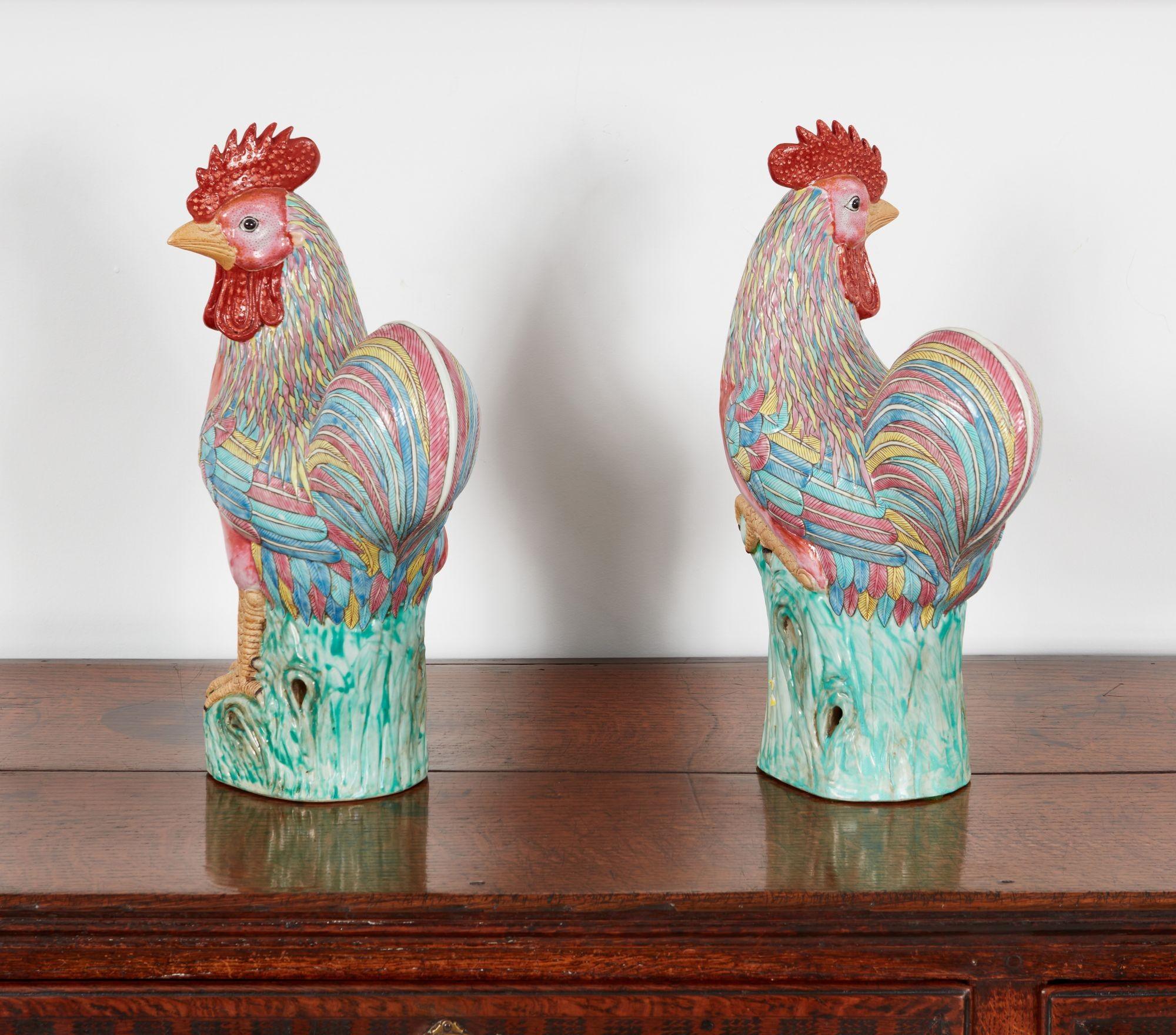 A pair of Chinese export glazed ceramic roosters with polychrome plumage in pinks, greens and orange with and striking red crowns and wattles, perched on weathered green striated tree stumps.