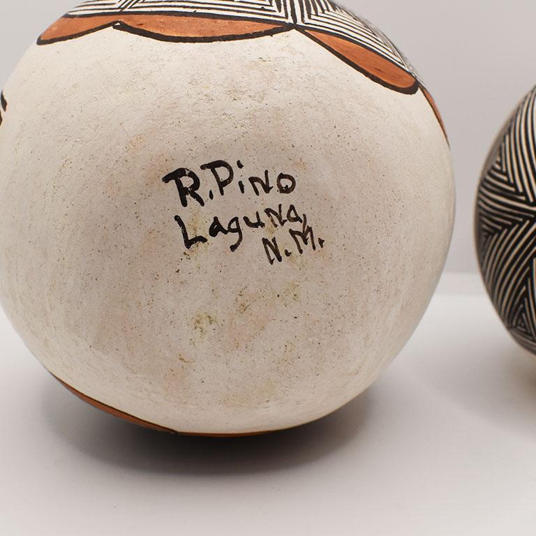 A pair of round Acoma pueblo pottery vessels. Each is decorated with intricate geometric designs and natural pigment paints of black, brown, and orange on white clay. They are handmade from native Acoma clay, and pit fired in the traditional