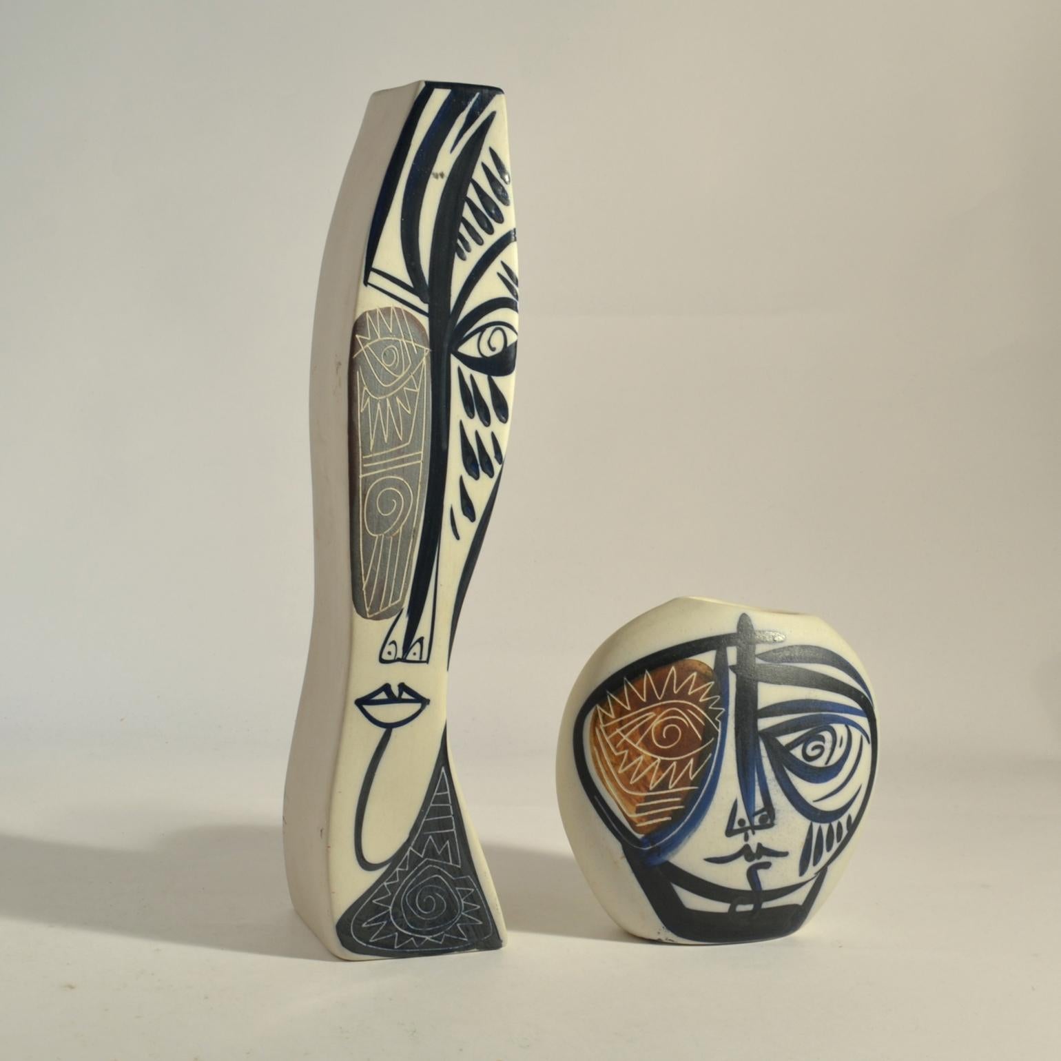 Two freeform white porcelain vases each have expressive brutalist face painted in ink blue, grey and brown strikes and part scratched into the glaze. They are both signed.
Dimensions:
Small vase; 16 x 16 x 7 cm
Tall vase; 40 x 9 x 8 cm.
 