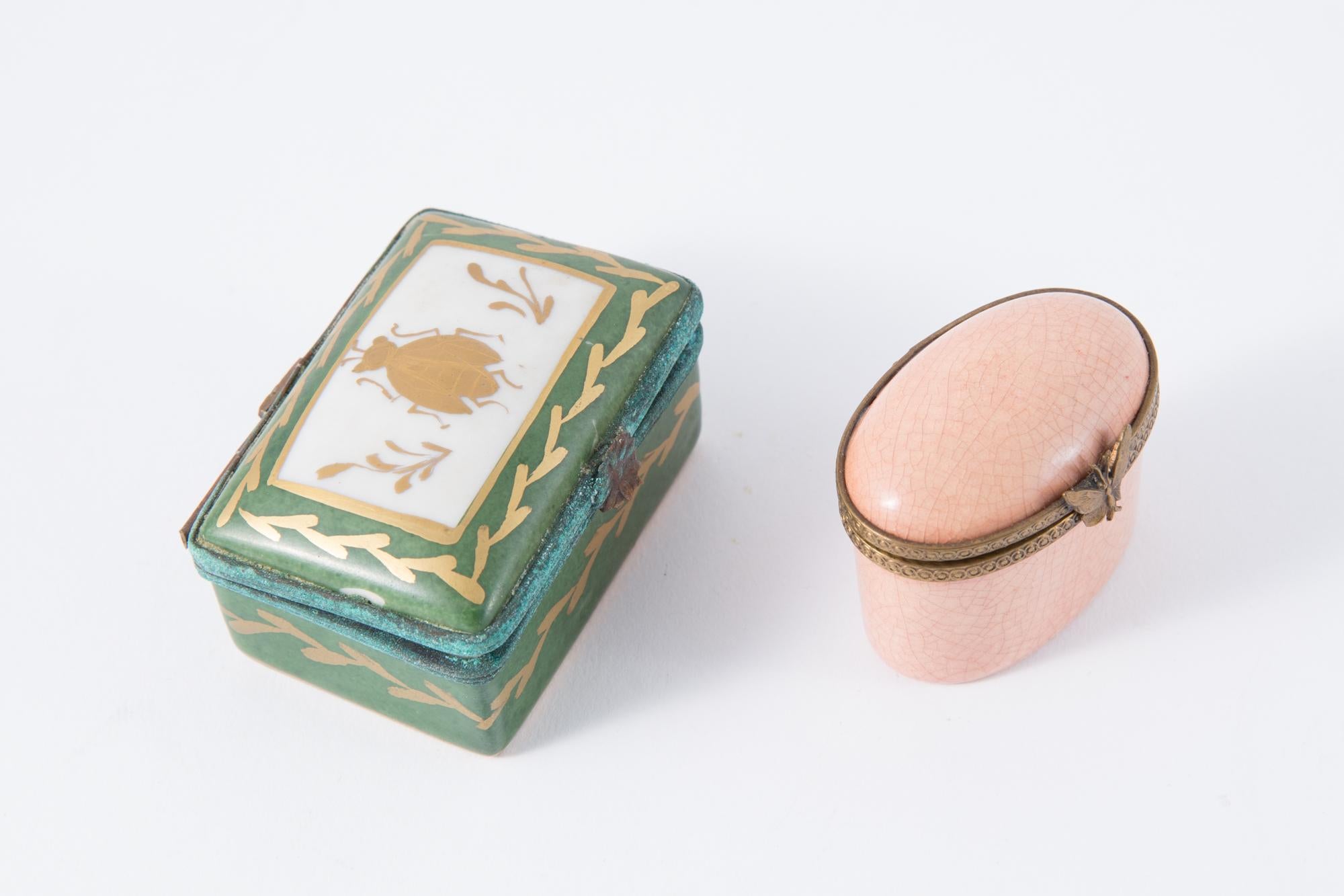 Two Porcelain pill or medicine box and metal frame decorated. The pink box gets a  a tarnish gold tone butterfly  on claps Long 5cm largeur 2.5cm hauteur 4cm,. The green box gets a decorative painted beatle on a tarnish flower claps opening ( no