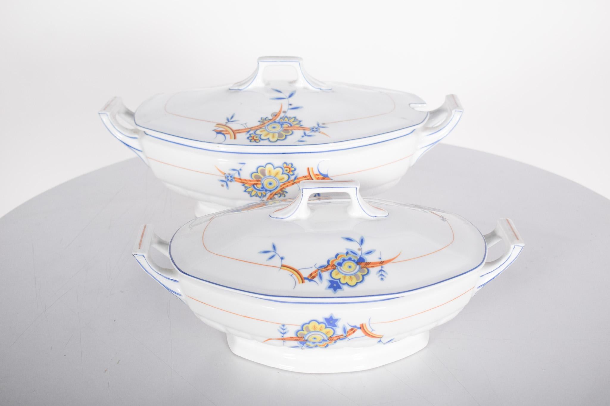 Deux soupières en porcelaine de Vista Alegre. Décorée de motifs floraux en bleu, orange et jaune.
Les pièces ont un design classique et harmonieux, avec des lignes douces et une forme allongée. Les couvercles sont dotés de poignées géométriques qui