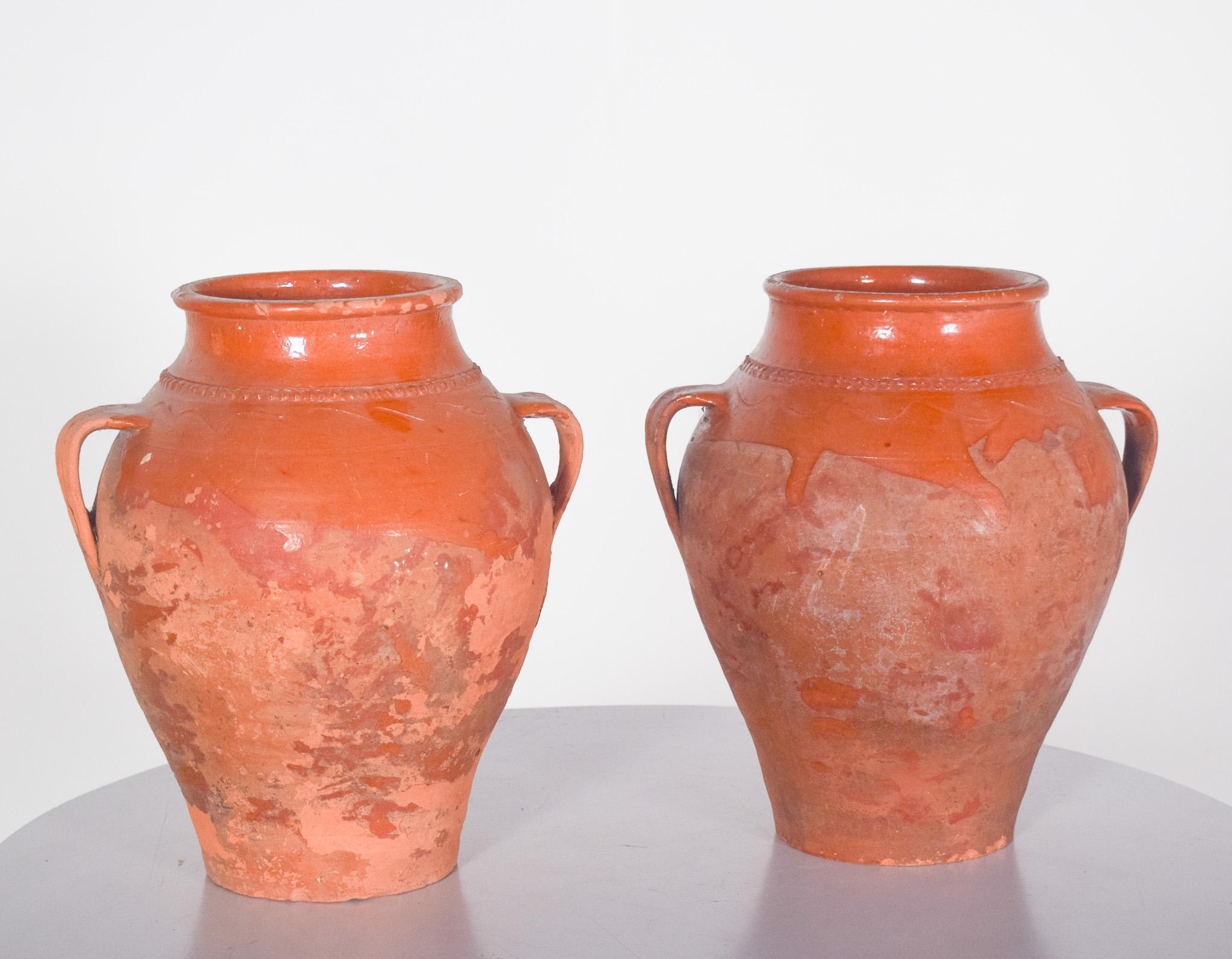 Two terracotta pots with handles. Two terracotta pots with handles. Handmade, with a rustic finish, domed shape and wide mouth, they have two side handles for easy handling. The surface has a reddish coloration characteristic of terracotta ceramics,