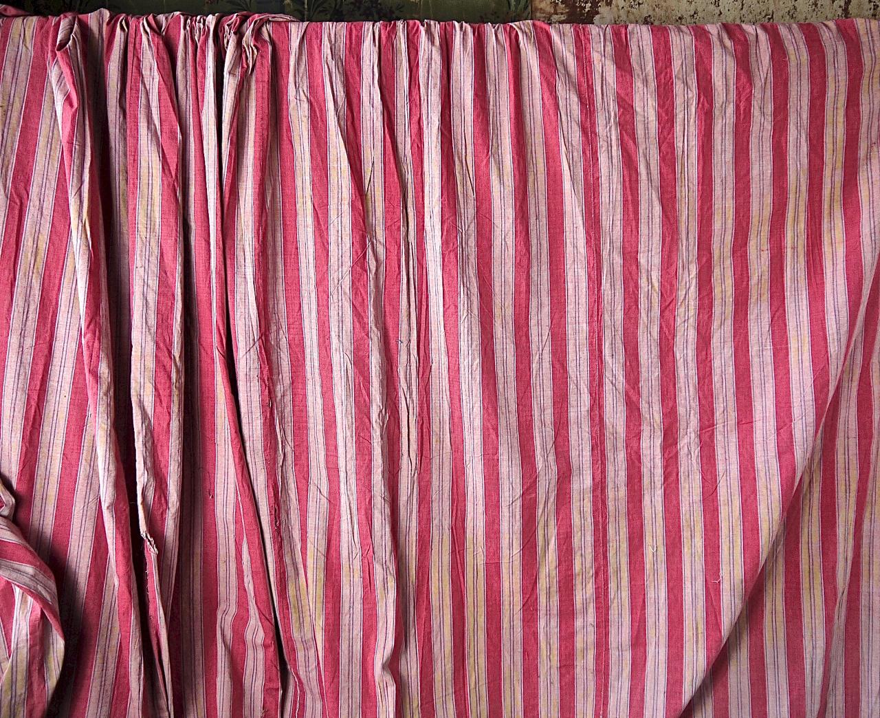 Late 18th century French soft red woven striped cotton large curtains that have a slight faded trace of yellow in some of the areas of the stripe. Trimmed along the side edges and across the gathered top. Some old repairs and small marks in a few