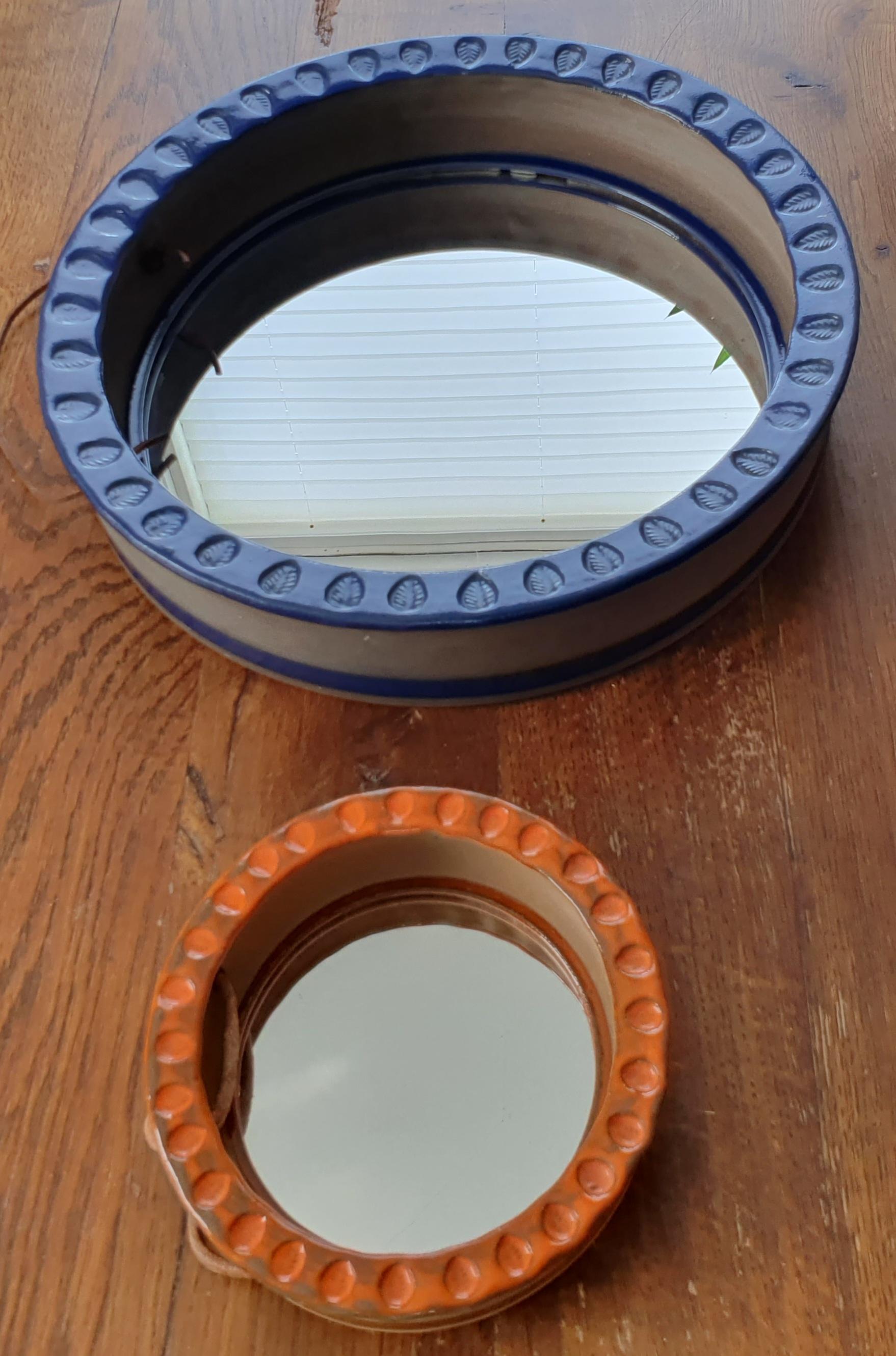 Two round ceramic mirrors by Danish Klavs Encke. Brown ceramic with strong blue and orange glaze. Blue large mirror measures 31 cm in diameter and is 6 cm high. Smaller orange mirror measures 14,5 cm in diameter and is 3,5 cm high. With leather
