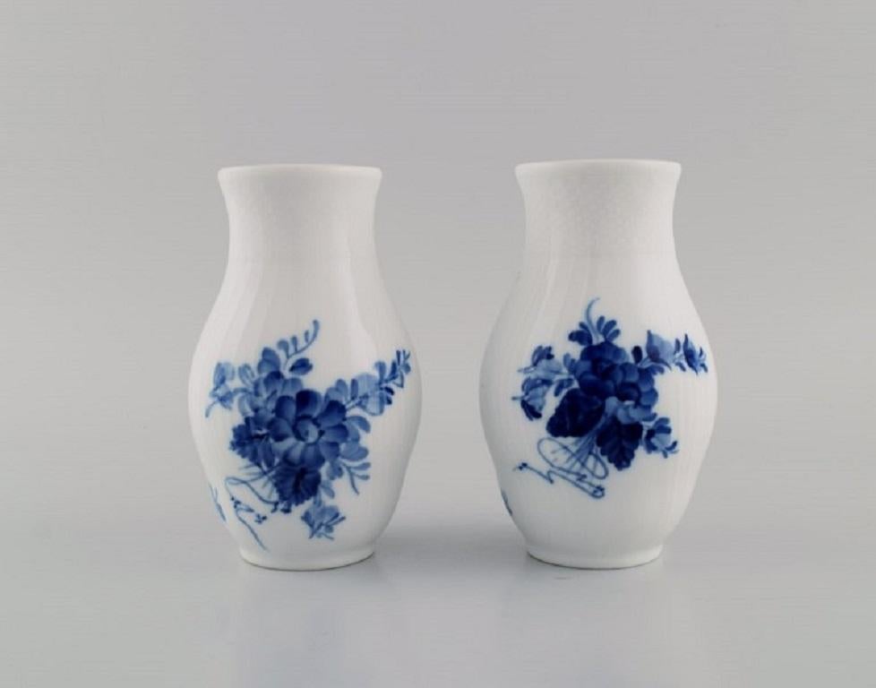 Dos jarrones curvos de flores azules de Royal Copenhagen. 
Model No. 10/1803. 
Con fecha de 1980-84.
Medidas: 14 x 8,5 cm.
En excelente estado.
Sellado.
1ª Calidad de fábrica.