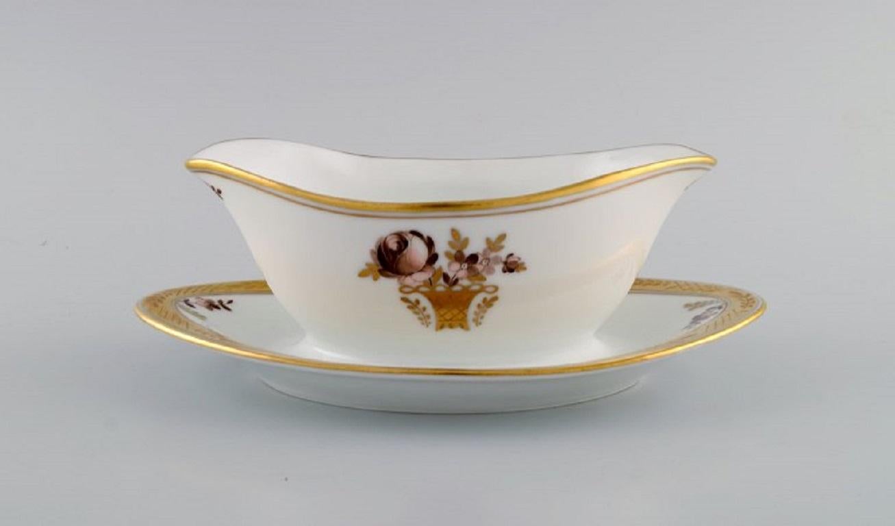 Two Royal Copenhagen golden basket sauce bowls in porcelain with flowers and gold decoration. 
Model number 595/9344. Early 20th century.
Measures: 22.5 x 13 cm.
Height: 8.5 cm.
In excellent condition.
Stamped.
1st factory quality.