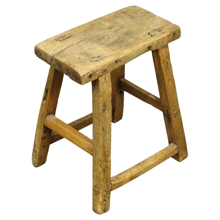 Dated to the early 20th century, this rustic stool has simple splayed-leg design and well-worn finish. Crafted of northern elm wood with mortise-and-tenon joinery, without the use of nails or screws, the stools feature a rectangular seat and four