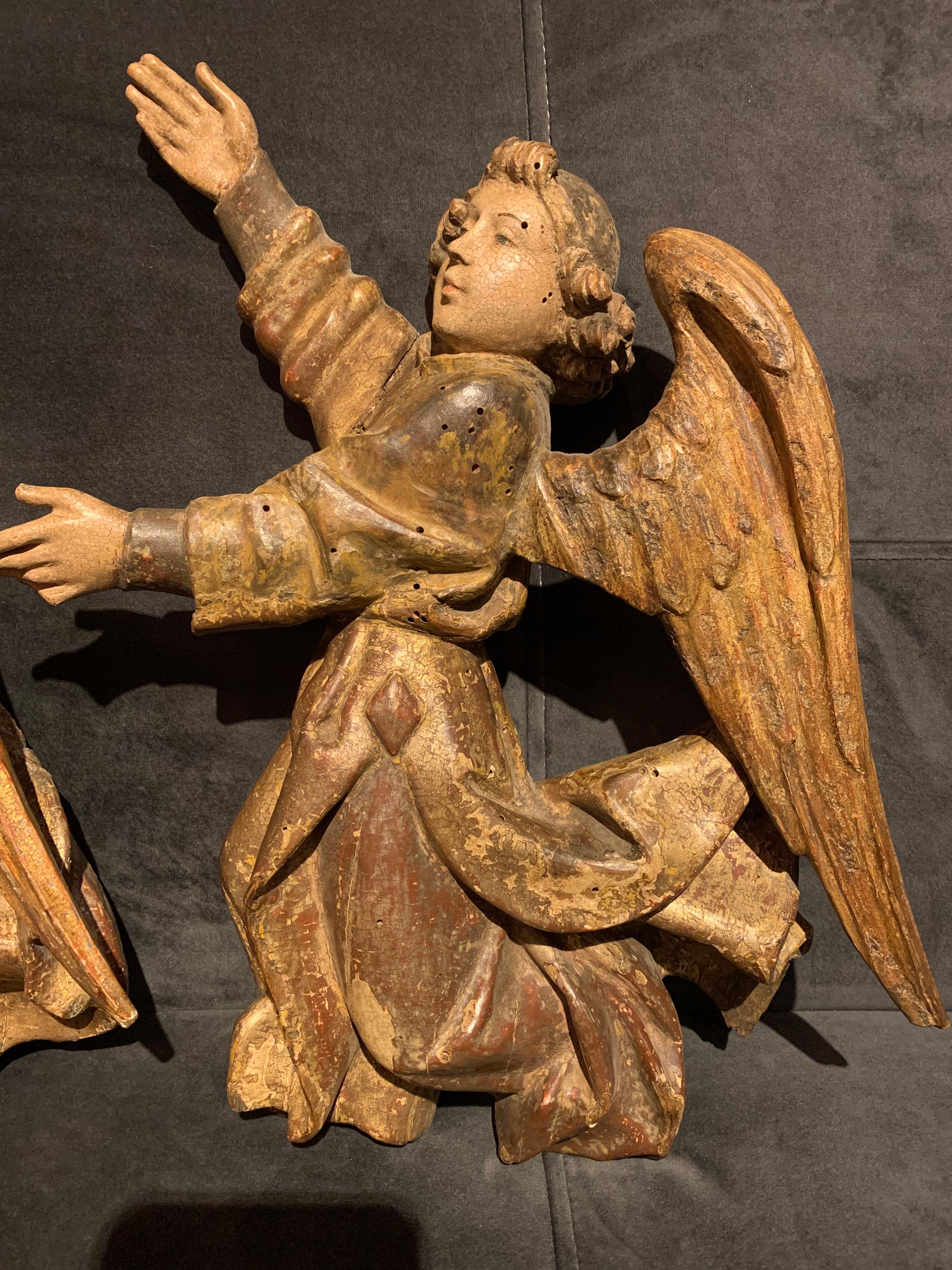 Two polychrome and gilt wood angels, sculpted in a high relief, representing a gesture of offering. 
No doubt they were part of a larger group, perhaps an altarpiece? 
The polychromy and the gilt are well preserved. Each one of them have a missing