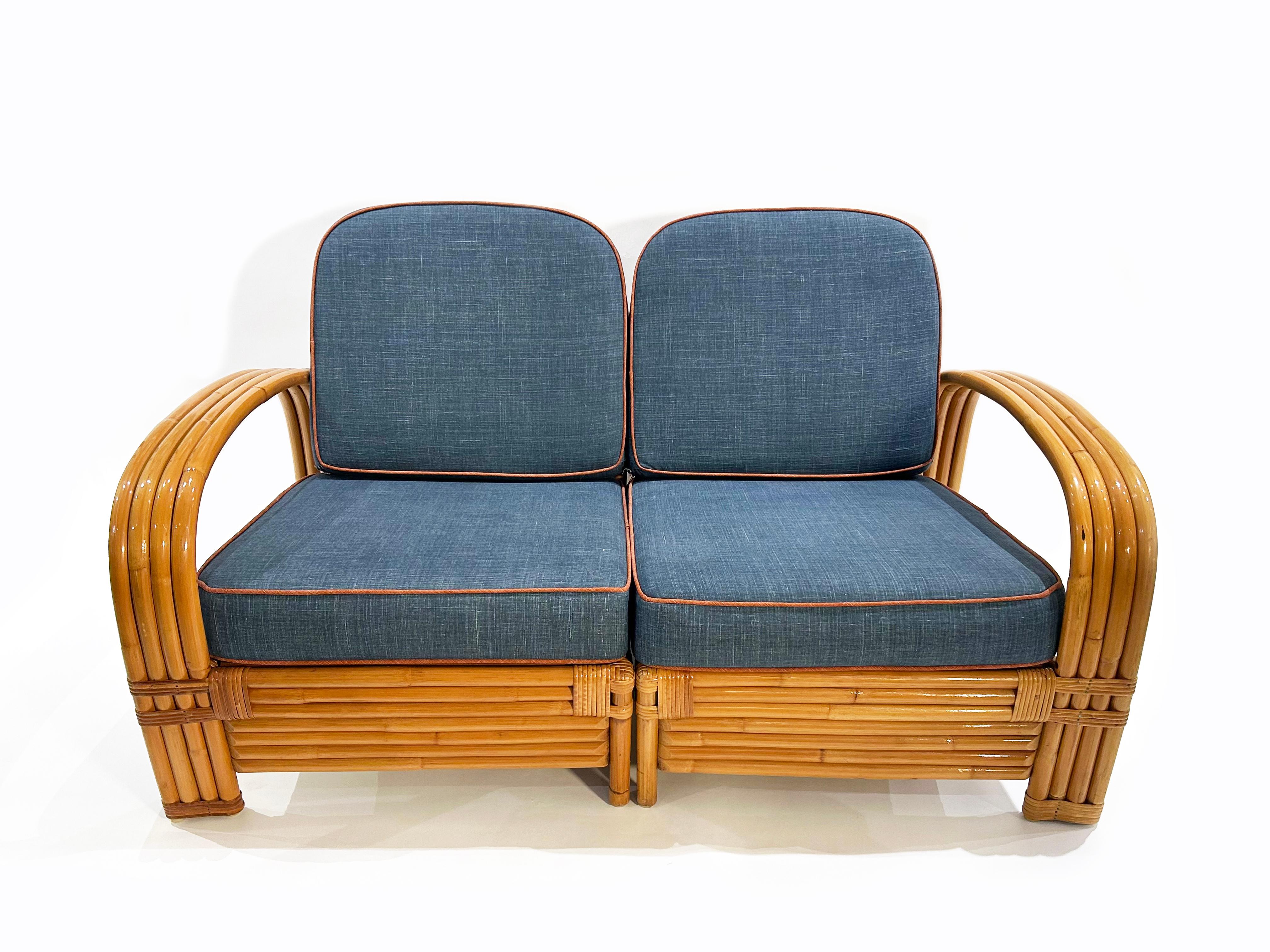 Sofá modular de dos plazas de ratán con cojines de tela azul y revestimiento de la base del asiento. Los cuatro cojines sueltos tienen un grosor de 4 3/8