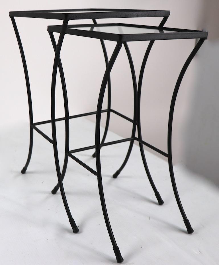 Two sets of nesting tables, of wrought iron with glass tops. Stylish midcentury tables, suitable for either indoor or outdoor use. Dimensions listing are for the larger table, priced and offered per set ( 1 nest of 2 tables ) but we would love to