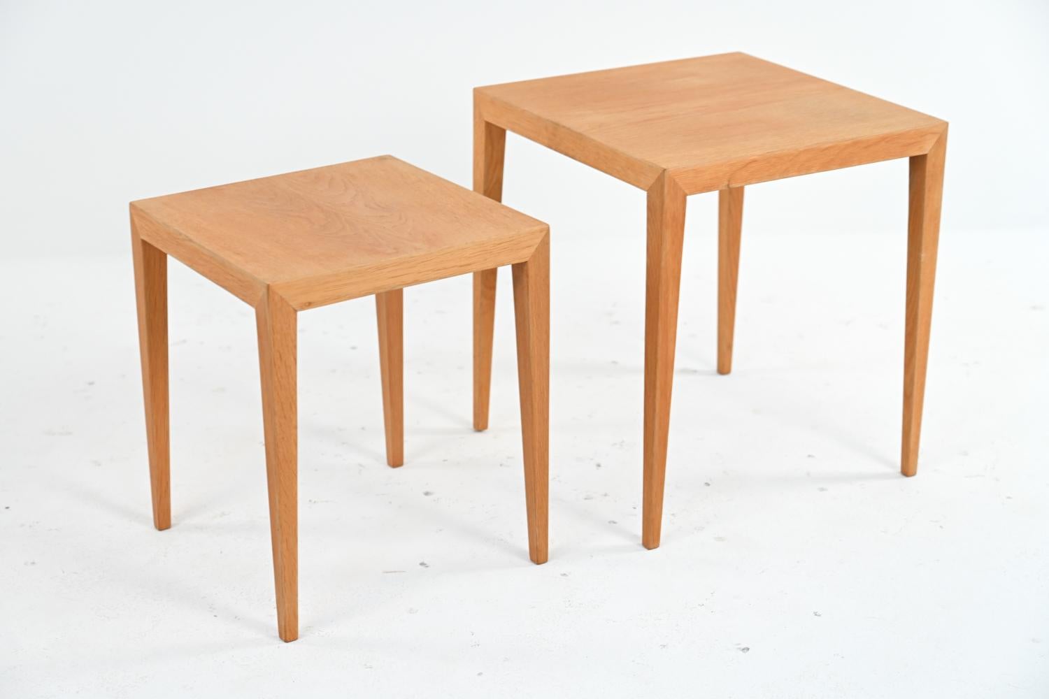 A set of two Danish mid-century nesting tables in blonde oak wood, designed by Severin Hansen for Haslev. These nesting side tables featuring Hansen's classic modern minimalist design with sleek tapered legs. One retains Danish control label
