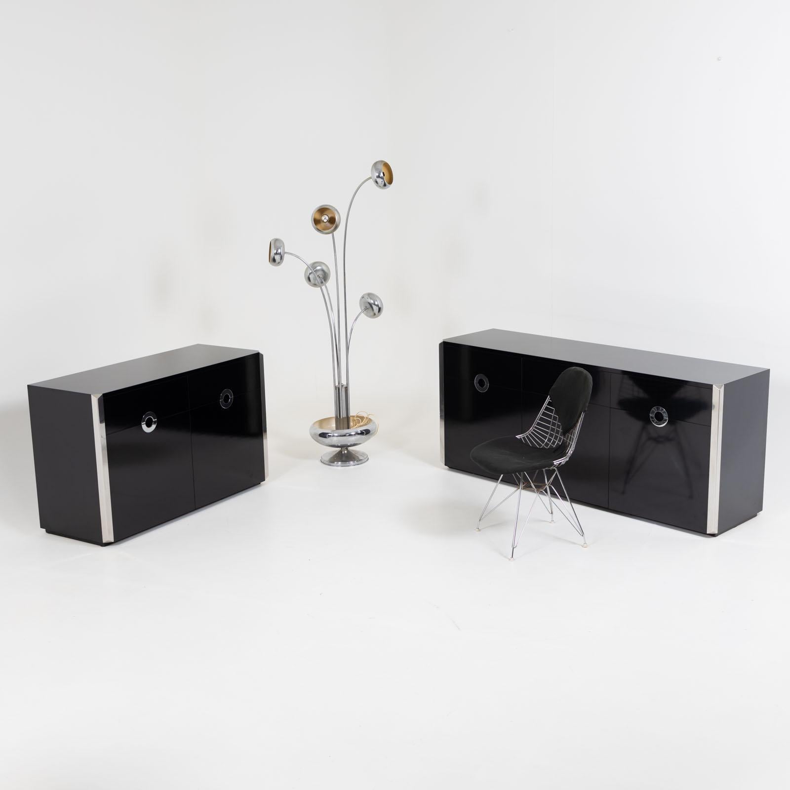 Two black sideboards by Willy Rizzo in two- and three-door versions with the characteristic contrasting edges in stainless steel and round handles. The middle door of the three-door version can be folded down. Dimensions of the smaller version: 76 x