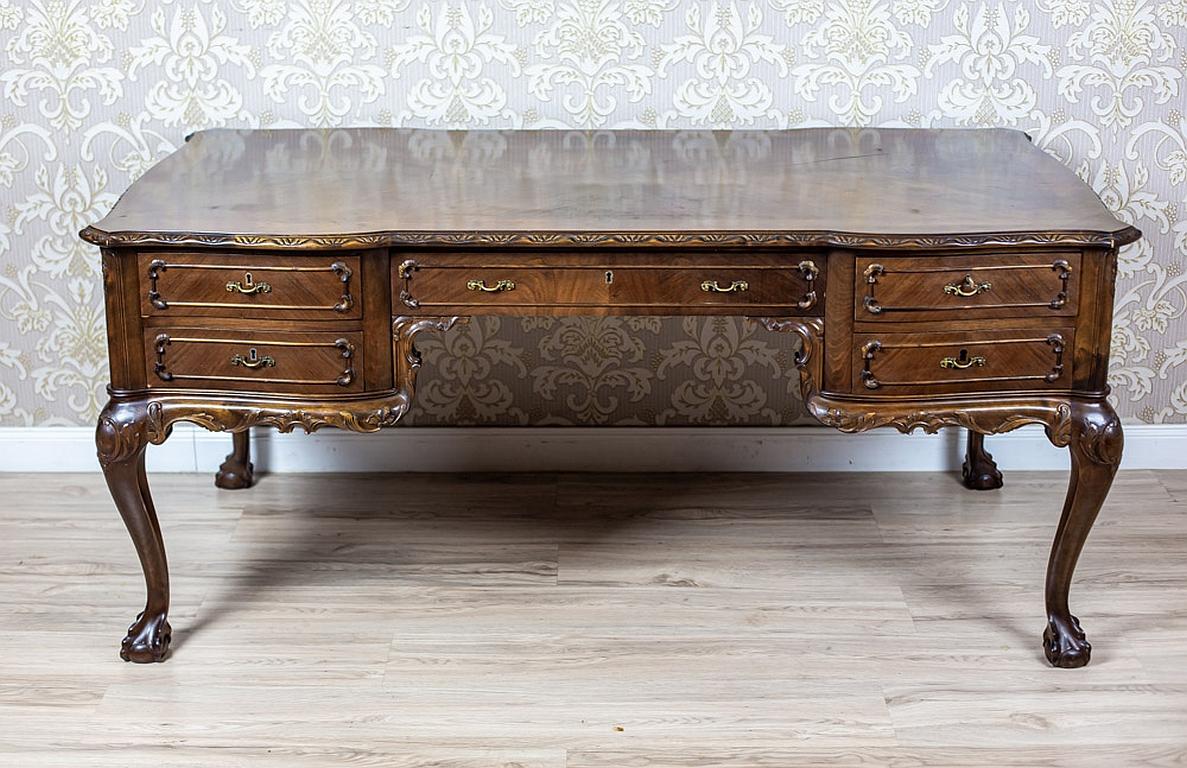 We present you a big wooden two-sided desk in the Chippendale type.
It was manufactured before 1945.
The whole is placed on high legs with prominent knees, which are decorated with carved patterns.
Moreover, the legs are finished with