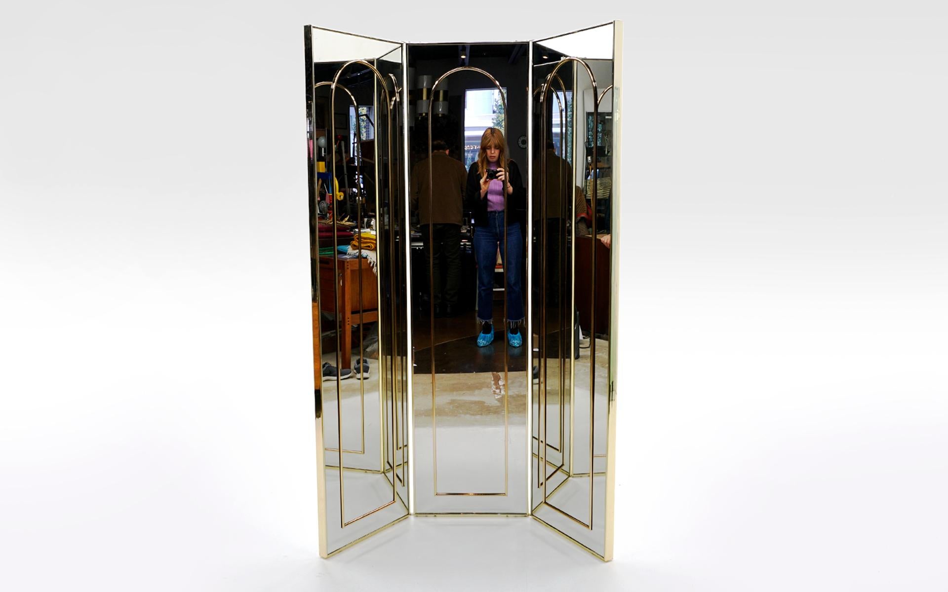 Tri-fold, two sided, floor standing dressing mirror, 1970s. Entirely framed in brass, one side has brass arch detail in the mirror and the other side is all mirror. The mirror can be folded either direction. Lots of options using this mirror as both