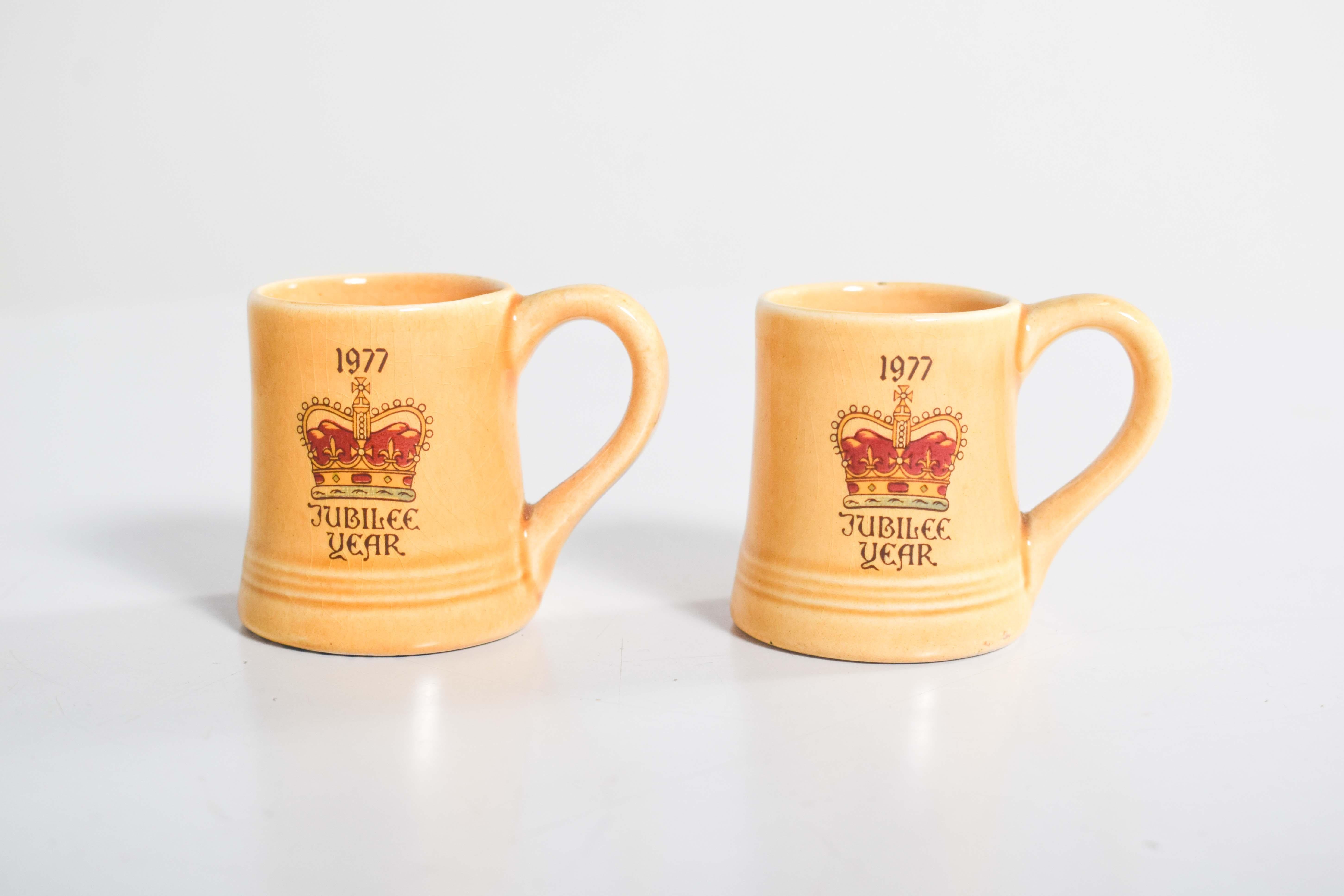 This pair of small yellow pottery mugs commemorates the 1977 Silver Jubilee of Her Majesty Queen Elizabeth II, celebrating 25 years of her reign. Each mug features a warm yellow glaze and a classic, sturdy design with a wide handle and ridged base.