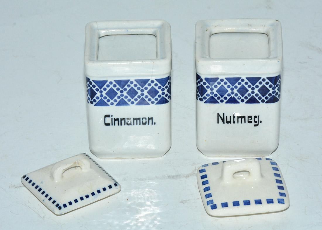 The two square vintage canisters hold nutmeg and cinnamon and have hand-painted designs in blue. Made of pottery. Stamped 