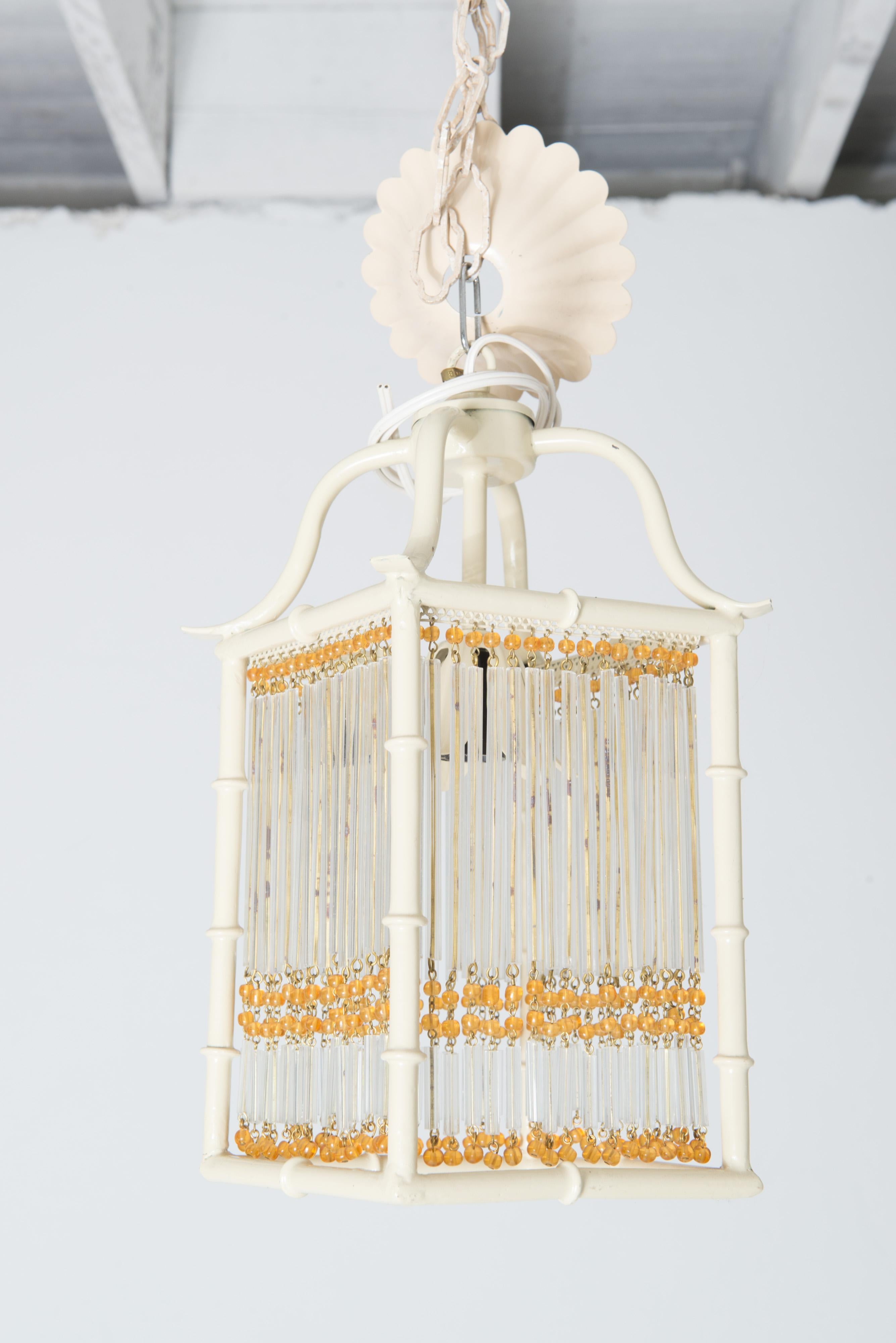 Il s'agit d'une paire de petites lanternes en métal peint blanc de style pagode en faux bambou.
Chaque lanterne Chinoiserie est ornée de perles de verre dorées et de tiges de verre transparent qui décorent les quatre côtés plats et ouverts de la