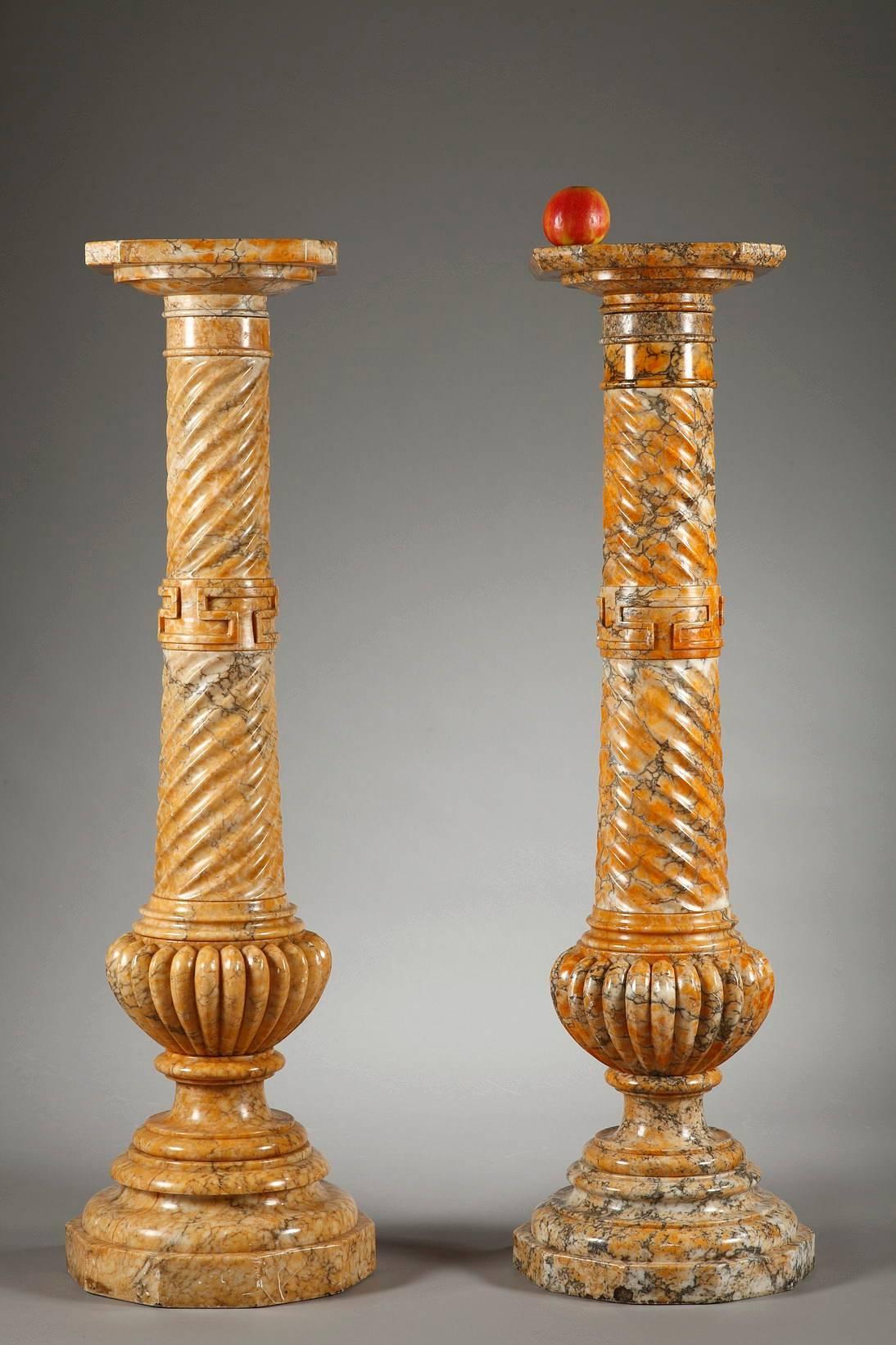 Two spiraling columns with Doric capitals in yellow sienna marble. Each column is decorated with Greek friezes and rests on a high, circular base with multiple terraced, beveled edges. Some small differences between the two columns,

 circa