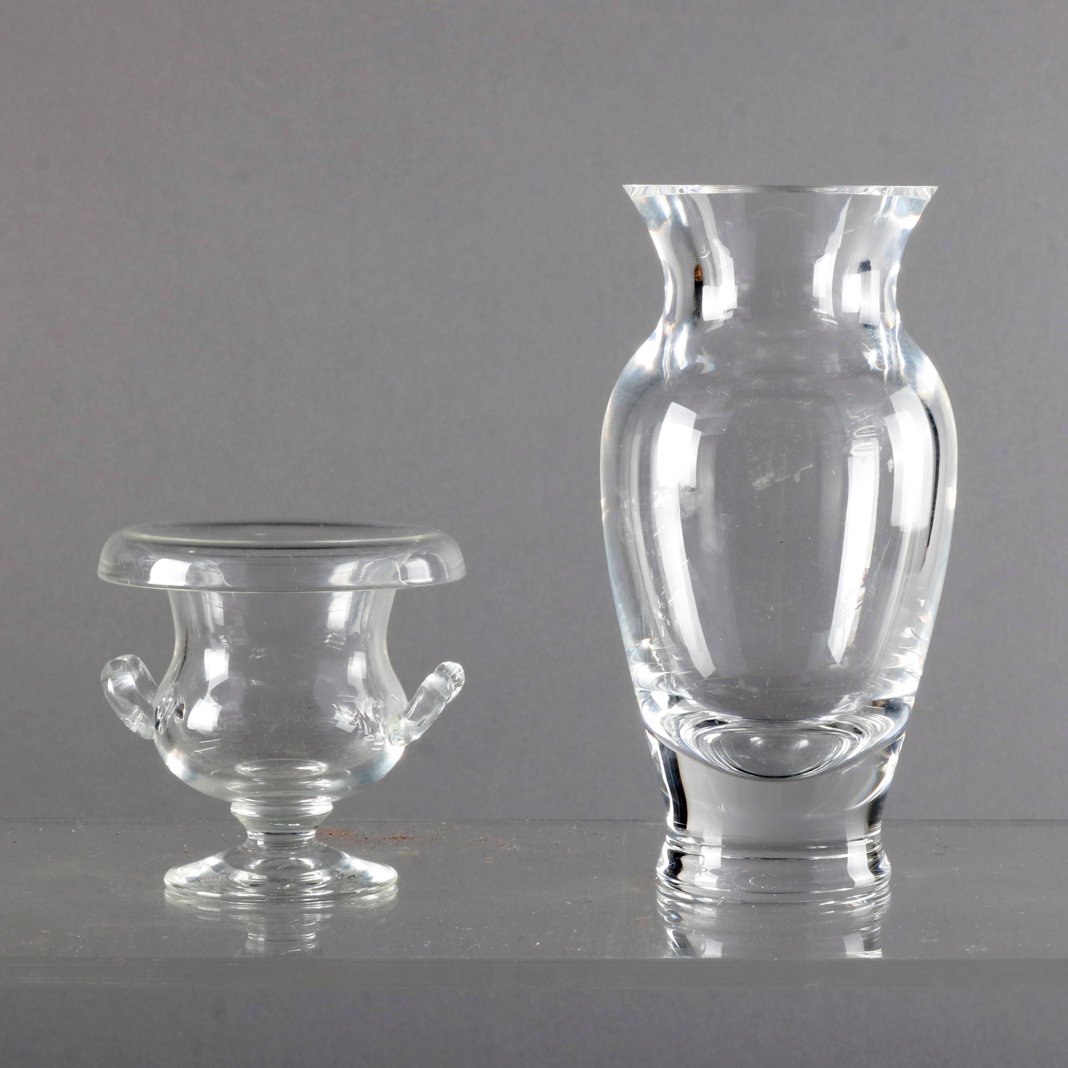 Two crystal vases by Steuben Glass Works offers one hourglass form vase signed on base and one urn form petite vase with rolled rim, double ribbed applied handles and raised on central plinth and unsigned, with box, 20th century


Measure -