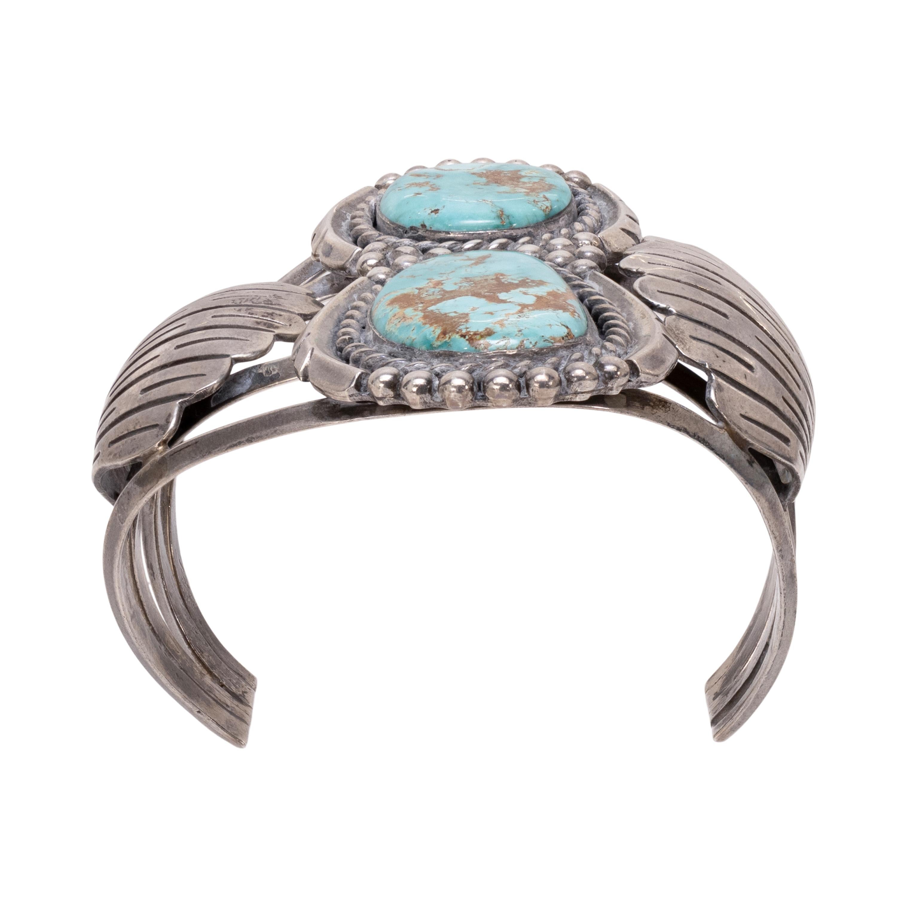 Bracciale Navajo a due pietre di turchese Cerrillos e argento sterling. Le pietre sono disposte in un'incastonatura verticale a forma di otto, ciascuna circondata da una corda intrecciata e da un bordo a forma di cappello con accenti di perline in