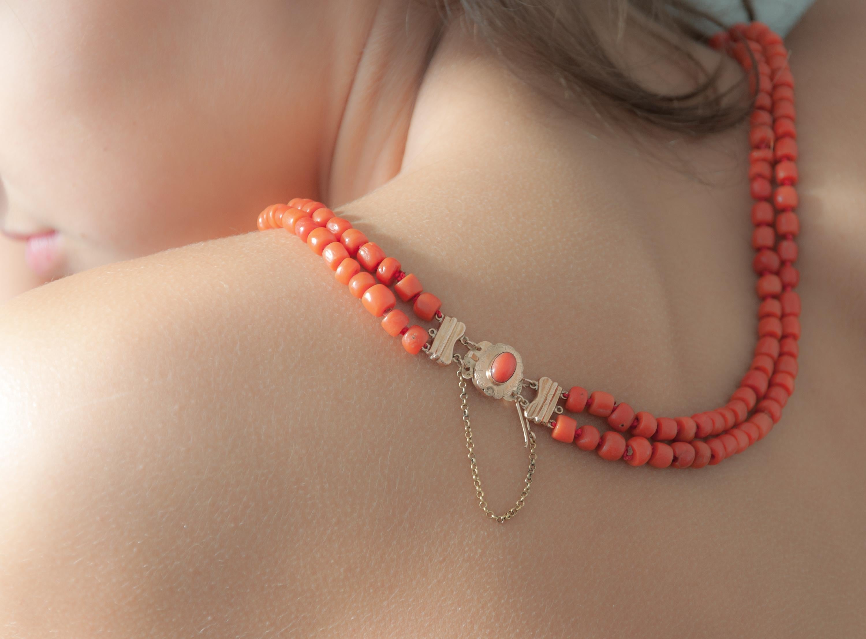Two-strand coral beaded necklace set with a beautiful oval-shaped gold clasp. The 14k gold clasp is made with an oval cabochon coral stone set in bezel setting. The coral beads are barrel-shaped and the cord is beautifully knotted between each