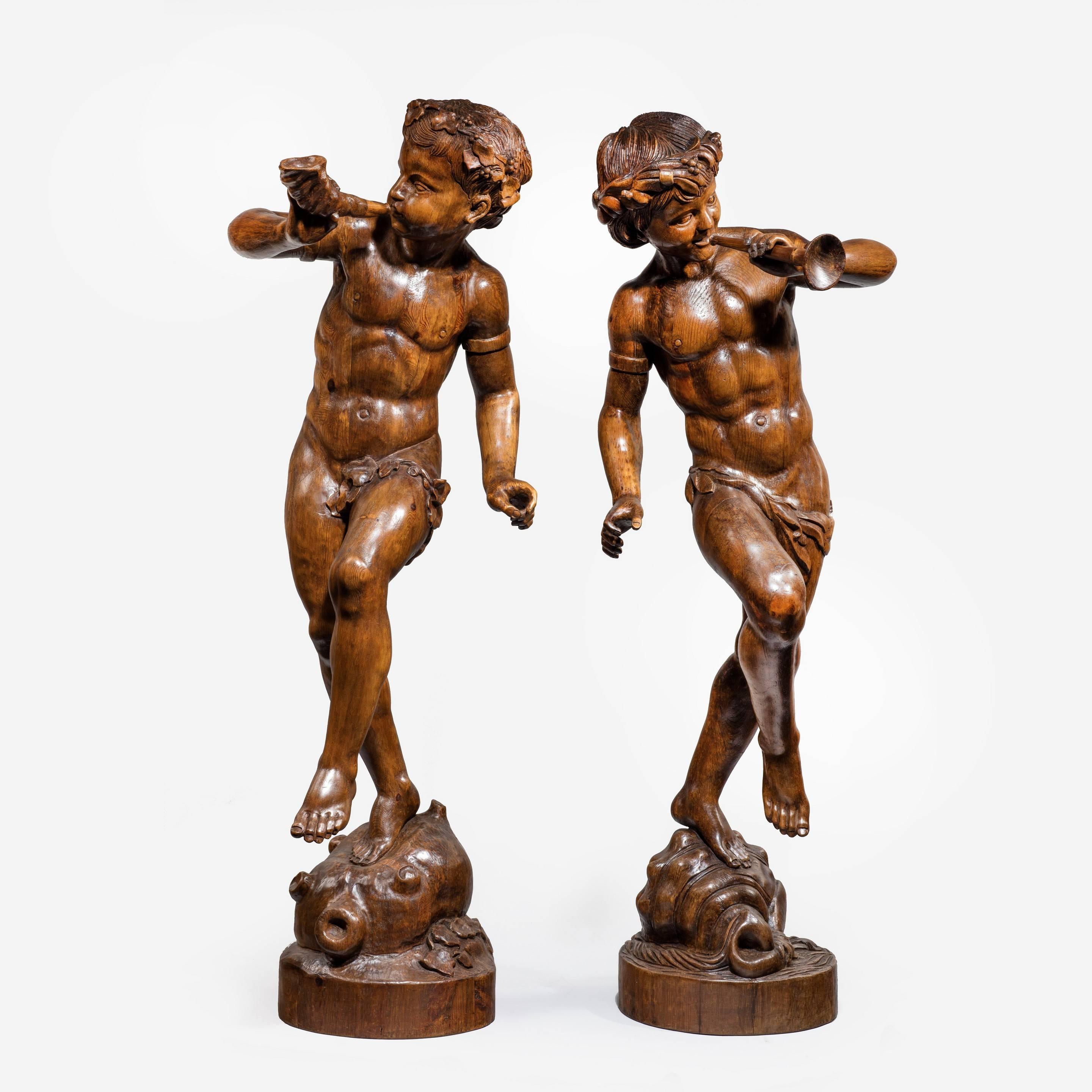 Two superb Italian pine Bacchanalian figures dancing with garlands in their hair,
one on a wine skin with a horn, the other on a shell with a trumpet.