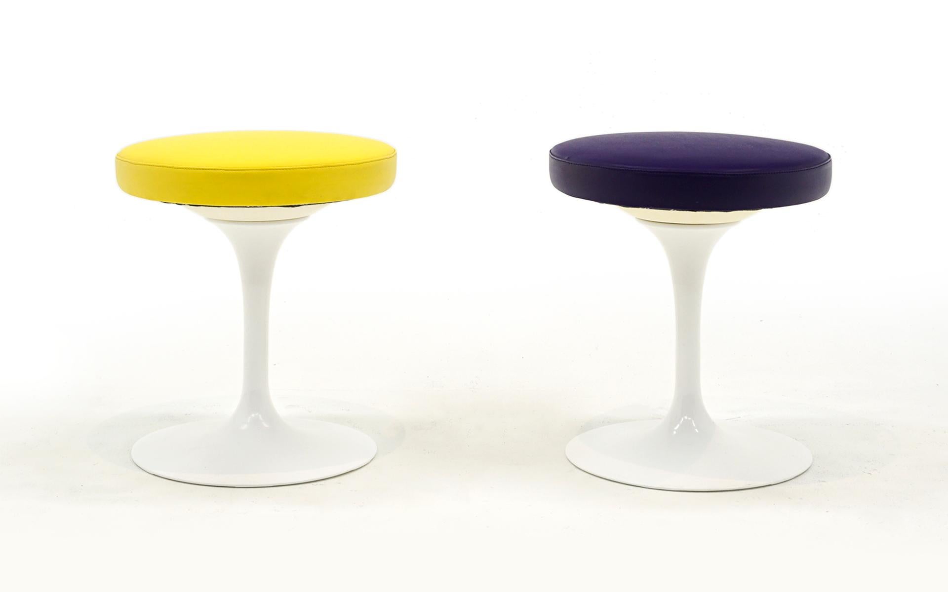 Pair of Eero Saarinen Tulip Stools, both with white bases, one purple vinyl seat and one with a yellow vinyl seat. Both appear to have been used very little if any. No visible scratches or chips to the bases and no signs of wear to the seats. Both