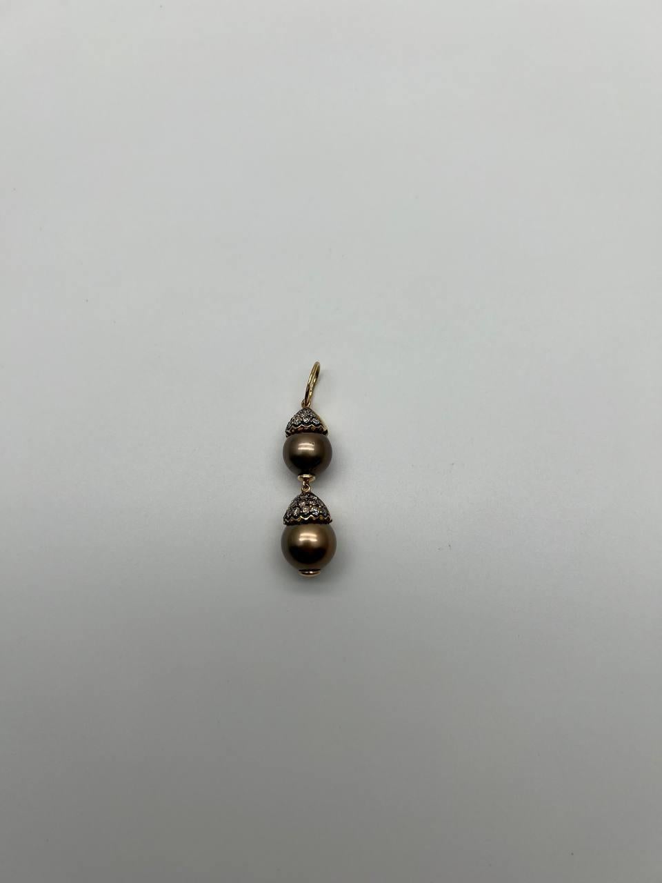 Cette élégante breloque présente un design captivant avec deux riches perles brunes et noires de Tahiti. Chaque perle est gracieusement ornée d'un travail métallique complexe, ajoutant une touche de sophistication. Complément idéal de toute