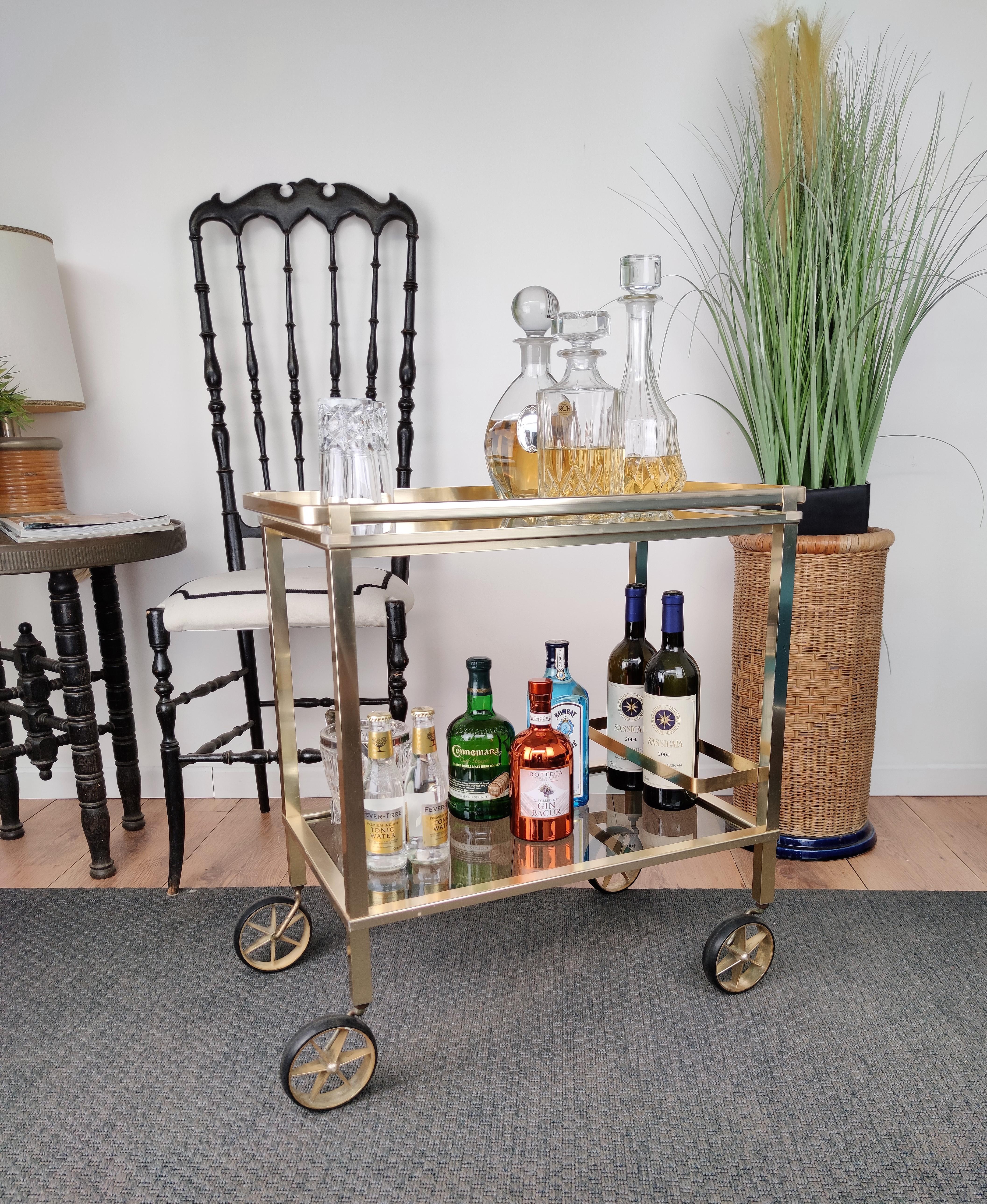 Beautiful and stylish vintage 1970s Italian two-tier brass and glass bar cart with removable top tray and frame for bottle holder. Very good condition.

A great piece that perfectly adds to every home decor the typical glitz, glamour and gold of