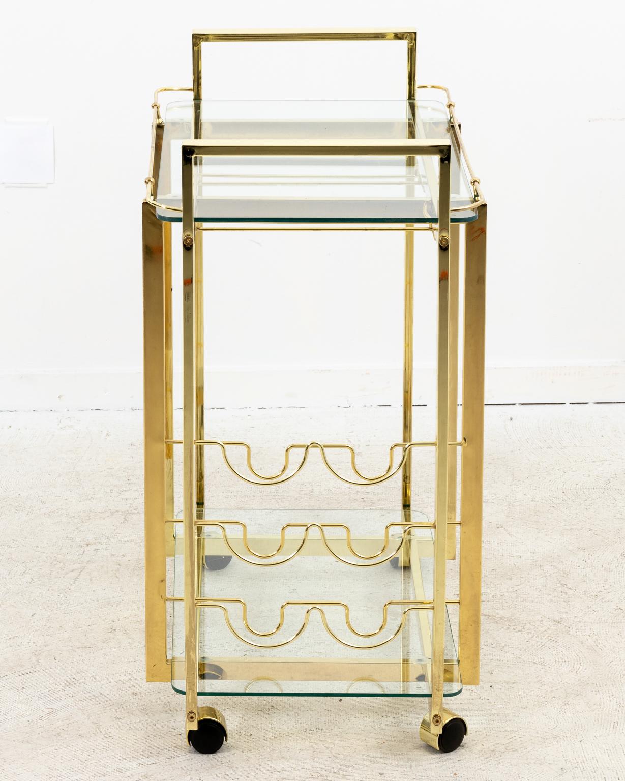 Modern style two-tier brass bar cart with glass shelves on casters in a polished finish, circa 1980s. The piece also comes with bottle racks. Please note of wear consistent with age including minor finish loss, oxidation, and surface scratches to