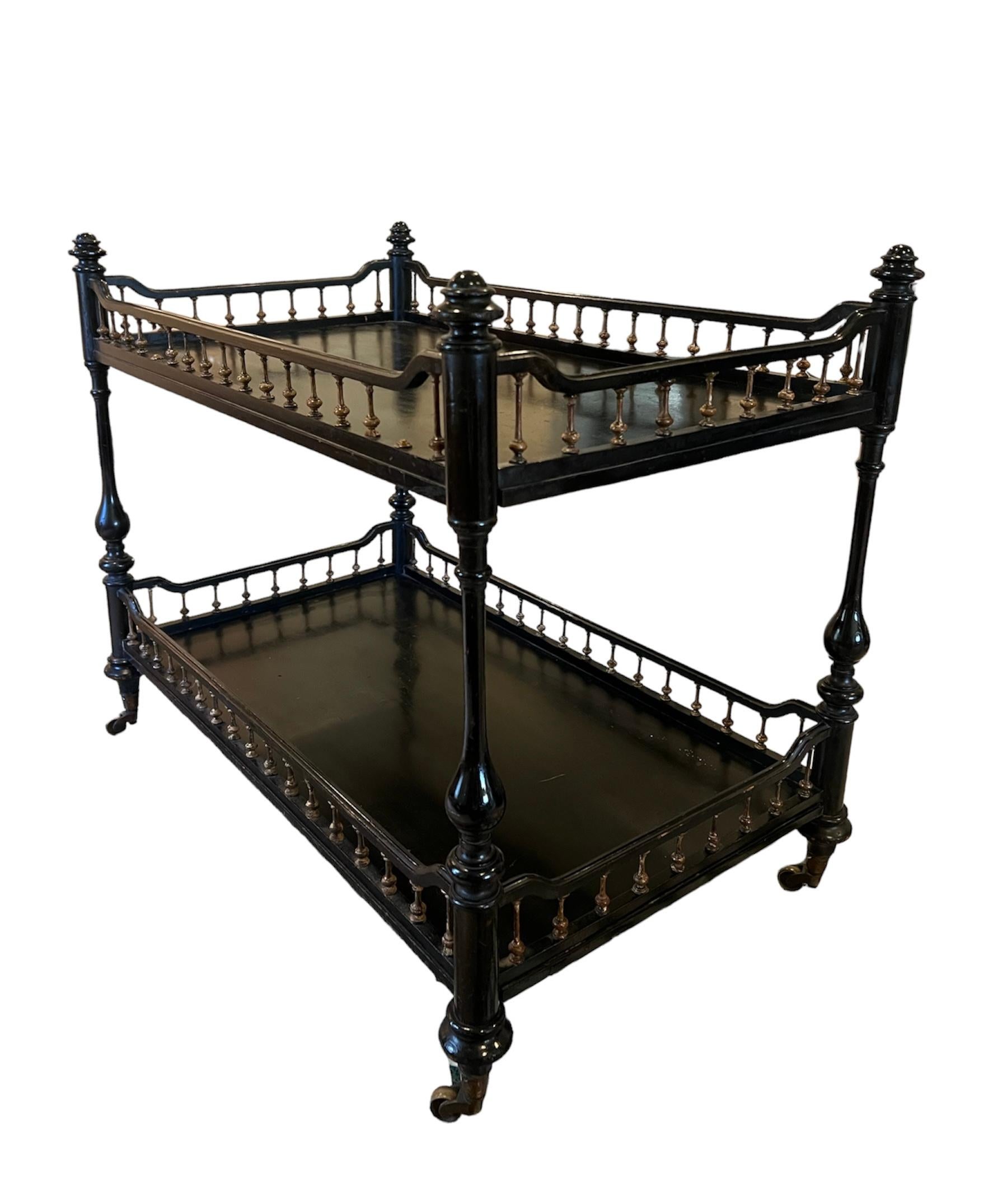 An exquisite two-tier étagère that exudes elegance and sophistication, perfect for connoisseurs of Victorian-era furniture with a touch of modern mobility. This stunning piece boasts an ebonized finish that gracefully contrasts with the delicate